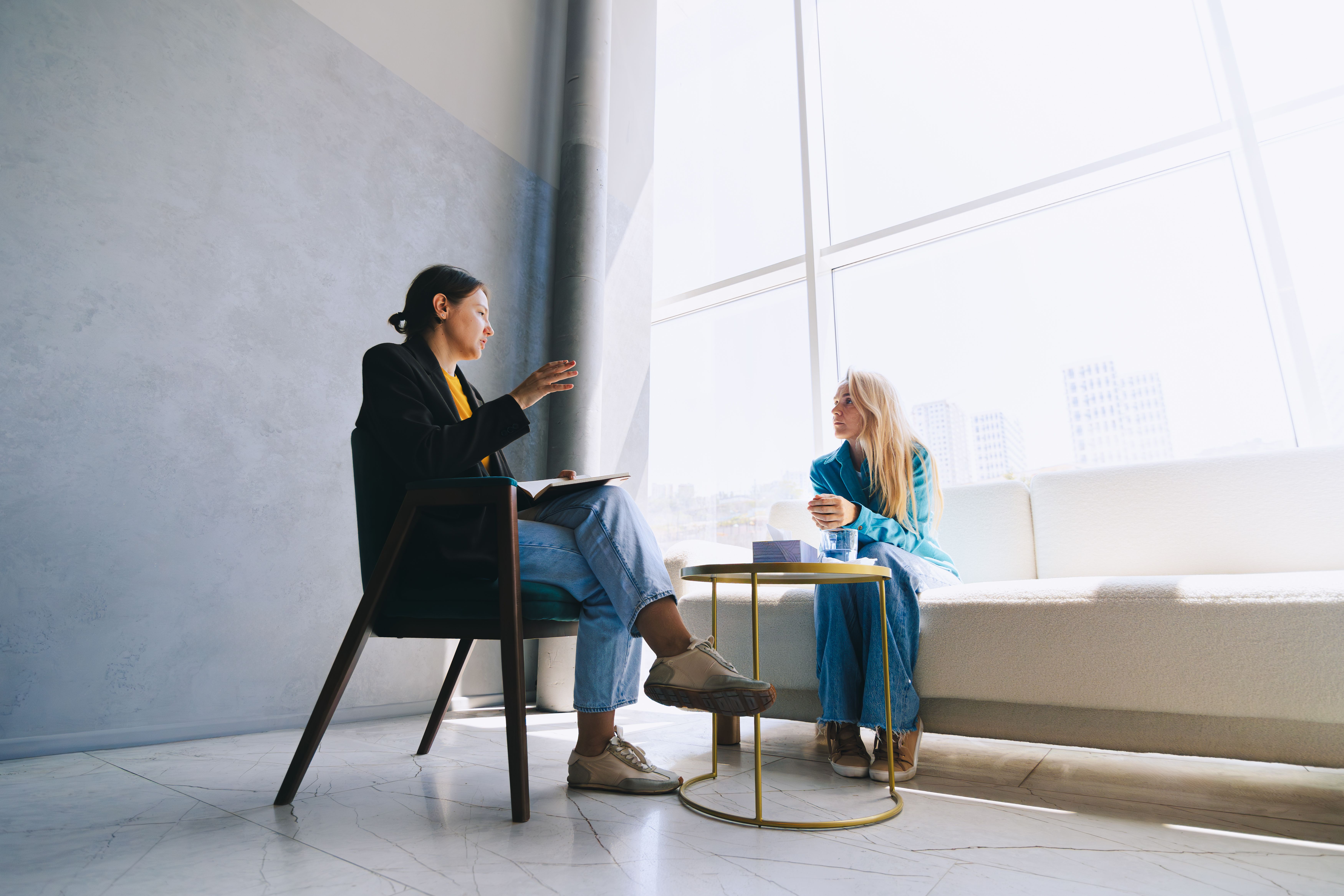 Two women sitting in front of large window having a business discussion.
