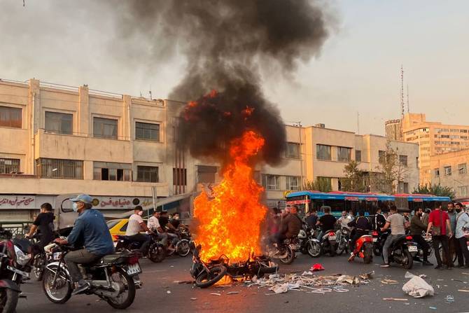 A picture obtained by AFP outside Iran, shows people gathering next to a burning motorcycle in the capital Tehran on October 8, 2022