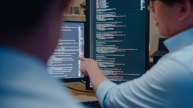 Programmers looking at and examining lines of code.
