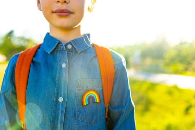 A child wears a denim shirt with a rainbow patch on it.
