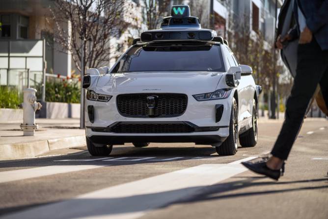 Image of pedestrians crossing a street in front of a Waymo driverless car.