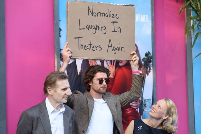 Someone is holding a sign with stars of The Naked Gun.