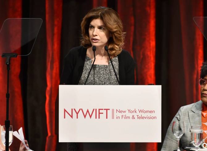 A brunette woman speaks at a podium.