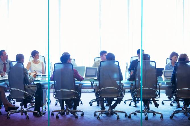 An image of a group of people sitting at a long table in an office environment. 