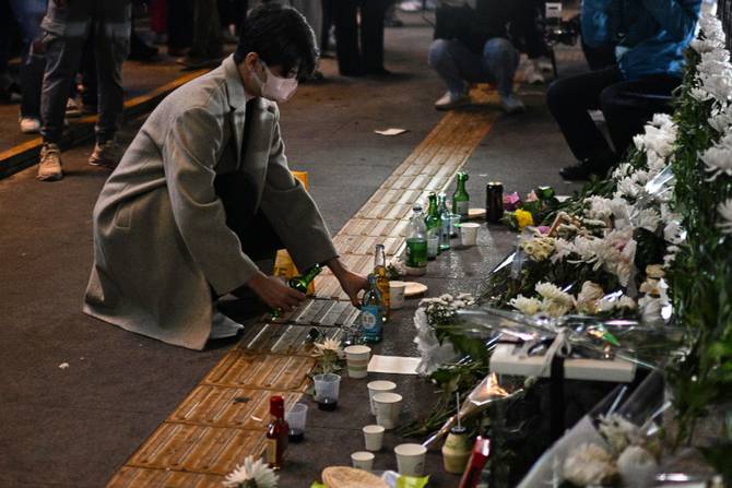 A man pours an alcoholic beverage in tribute to those who were killed in a Halloween stampede at a makeshift memorial outside the Itaewon subway station
