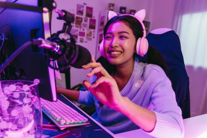 A smiling gamer in a pink headset looks at her computer screen