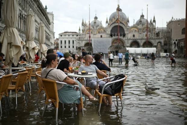 People stay at cafe terrace in a flooded St. Mark's square during high tide