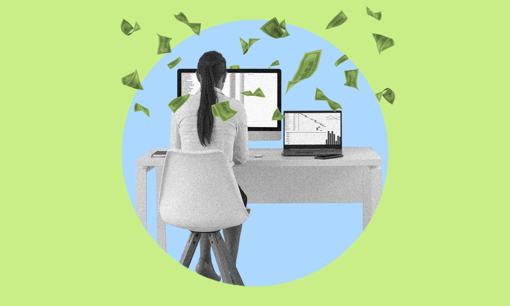 An office manager sitting at a desk in front of two computers with money floating around her