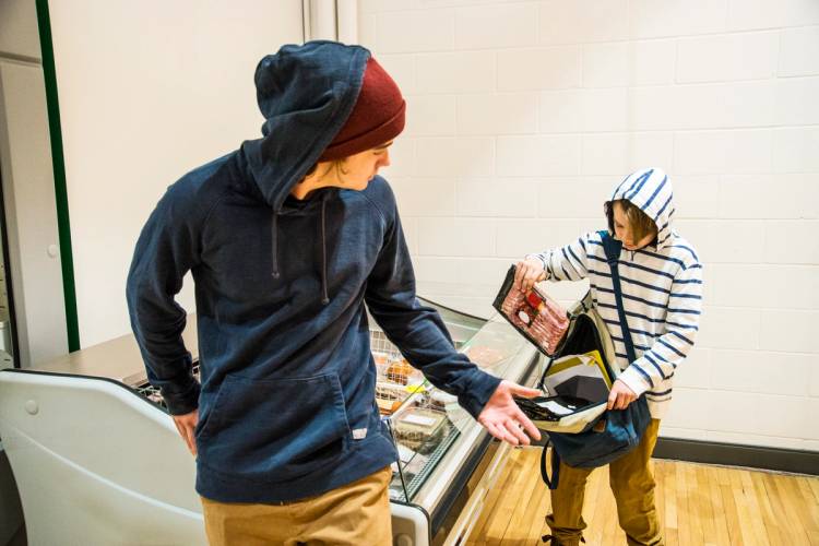 An adolescent boy secretly puts groceries into his knapsack. 