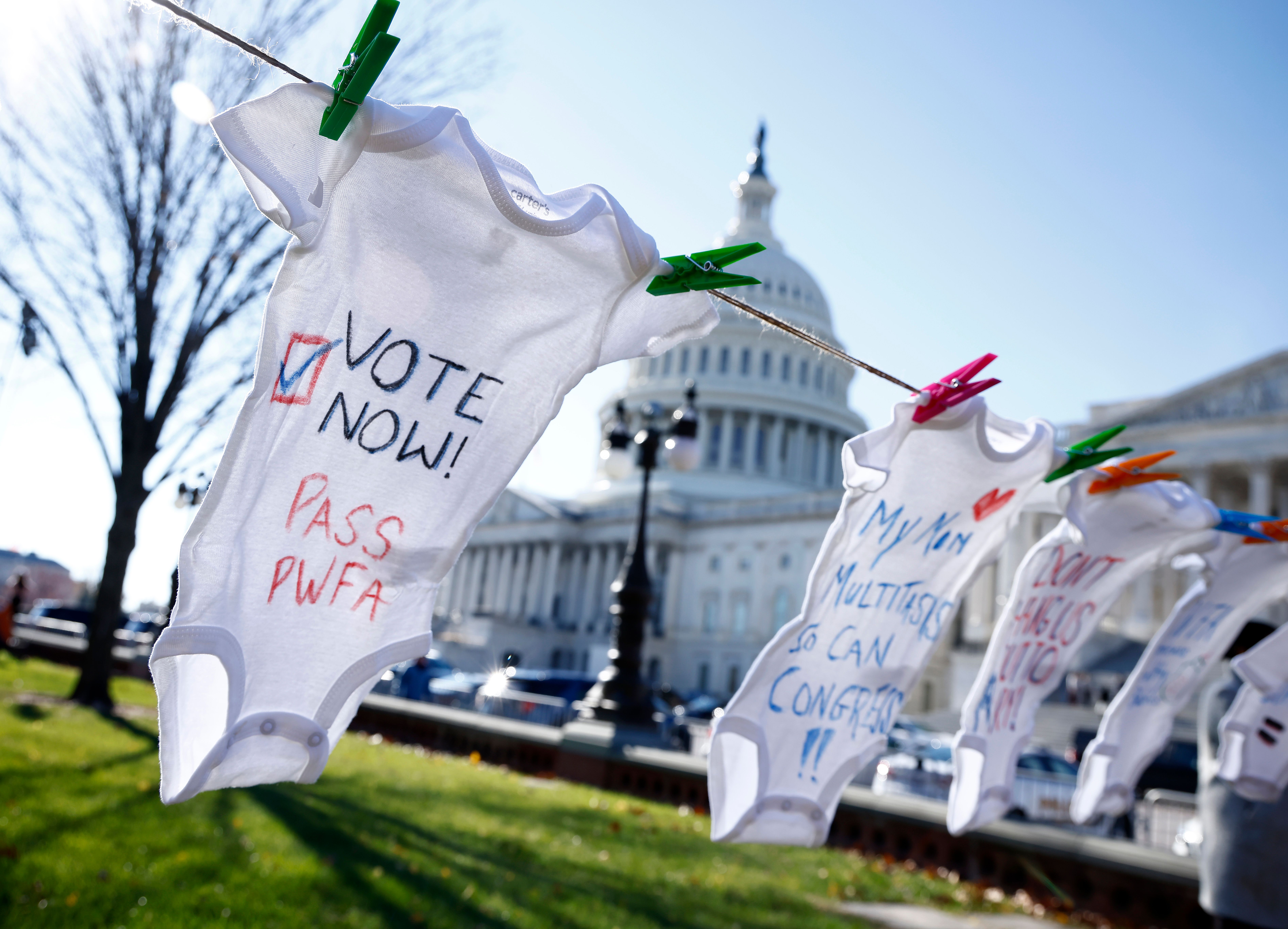 A white onesie reads "Vote now! Pass PWFA" in front of the US Capitol.