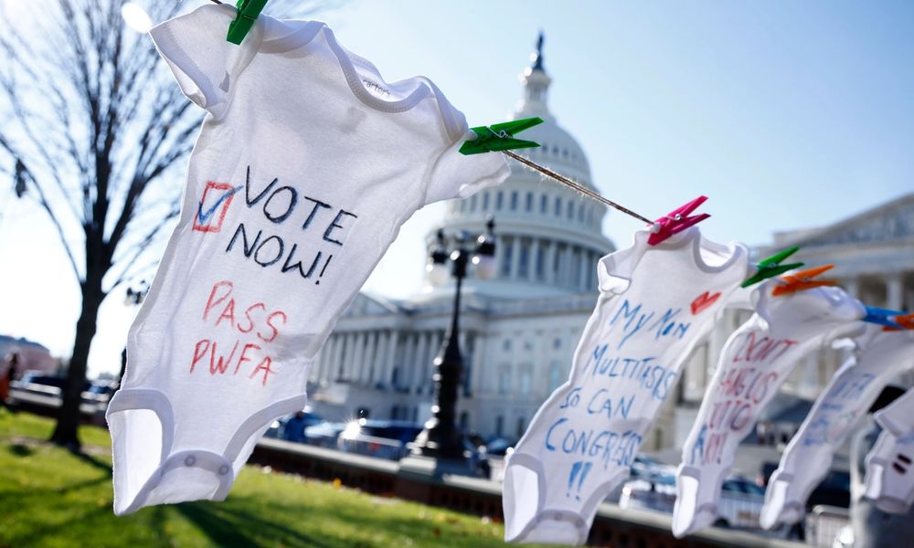 A white onesie reads "Vote now! Pass PWFA" in front of the US Capitol.