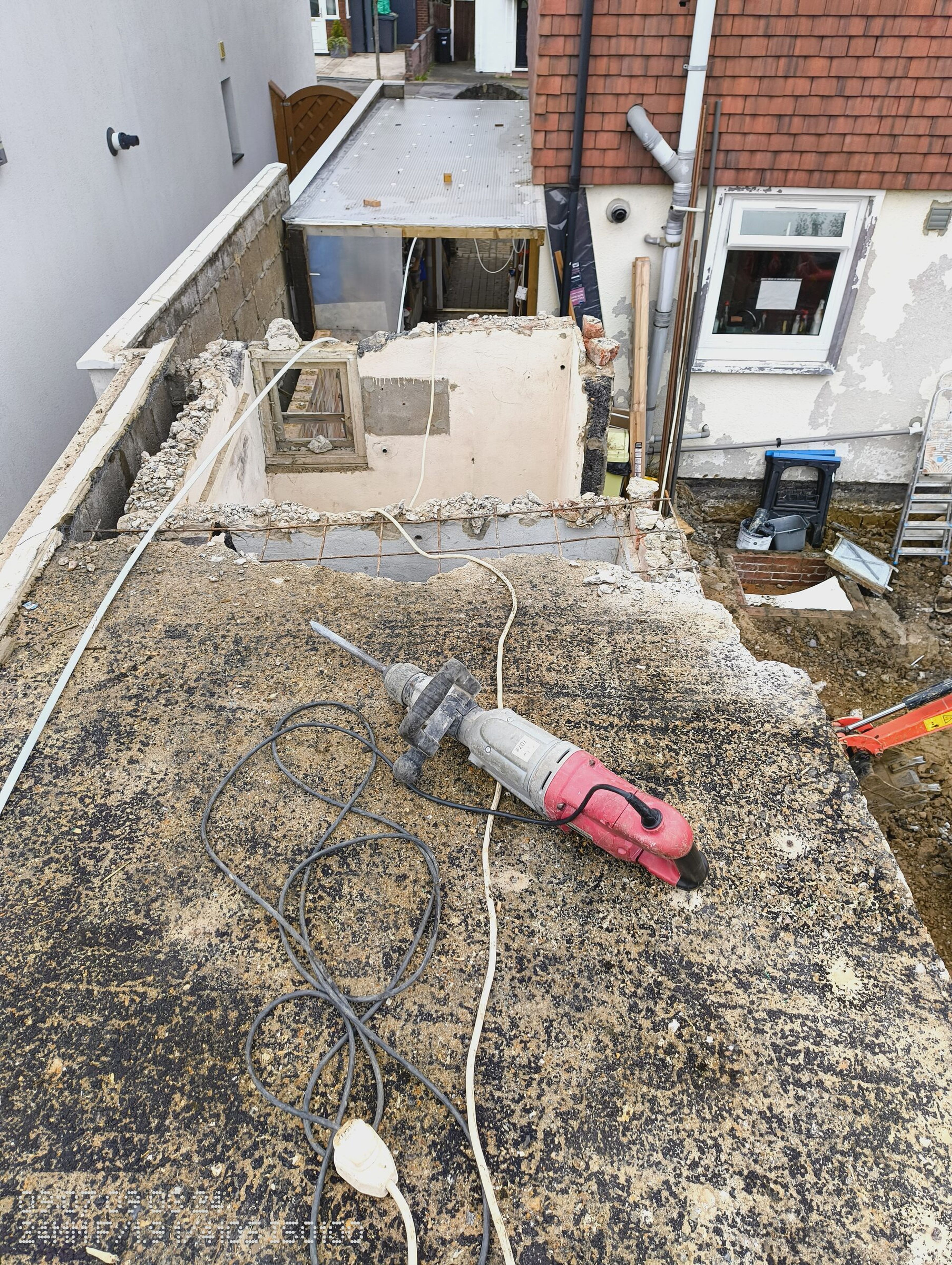 More of the concrete roof taken down, with a breaker on the slab and the digger working in the garden below.