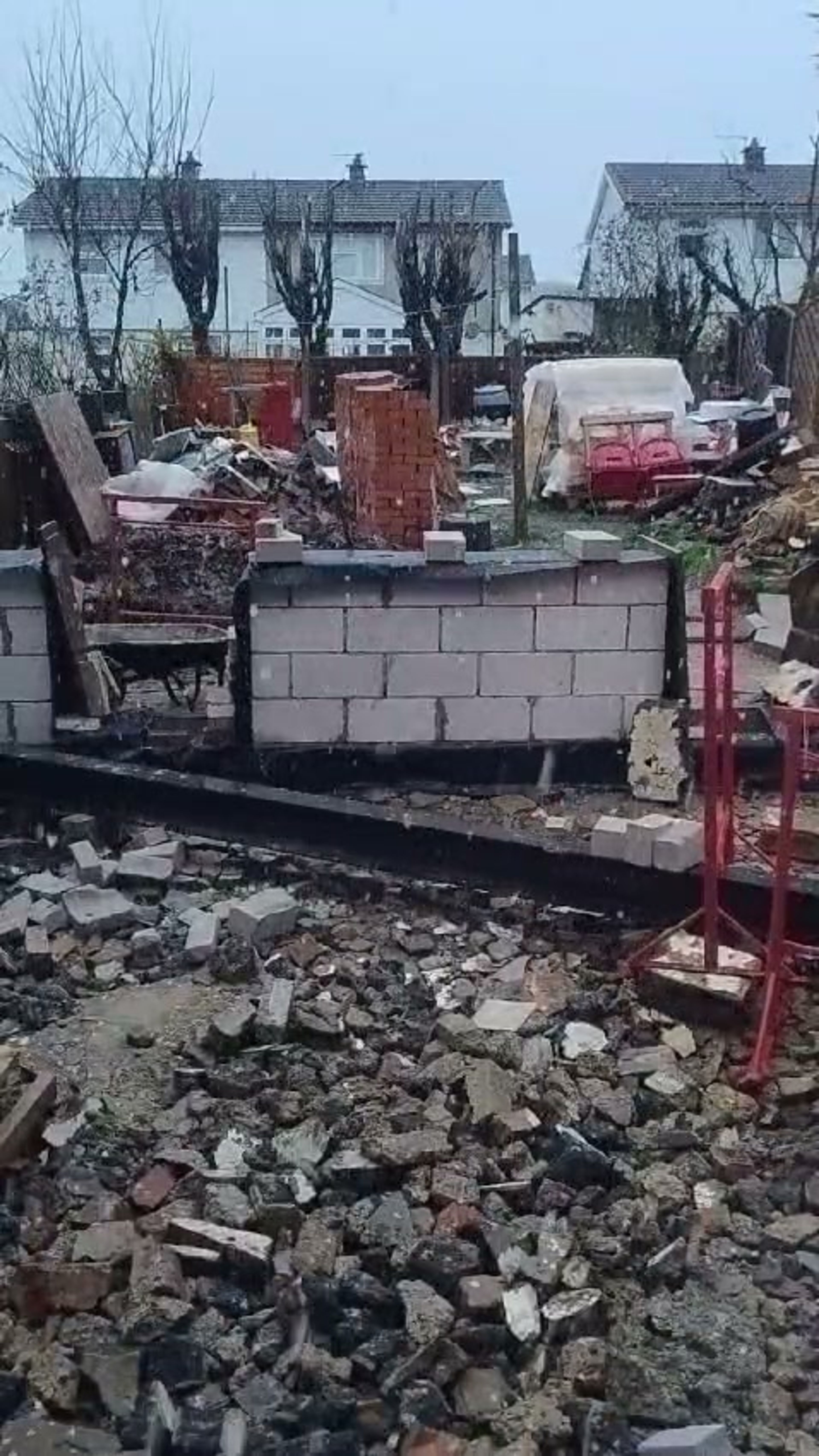New block walls of a rear extension in Chigwell, with rubble and a stack of bricks beyond