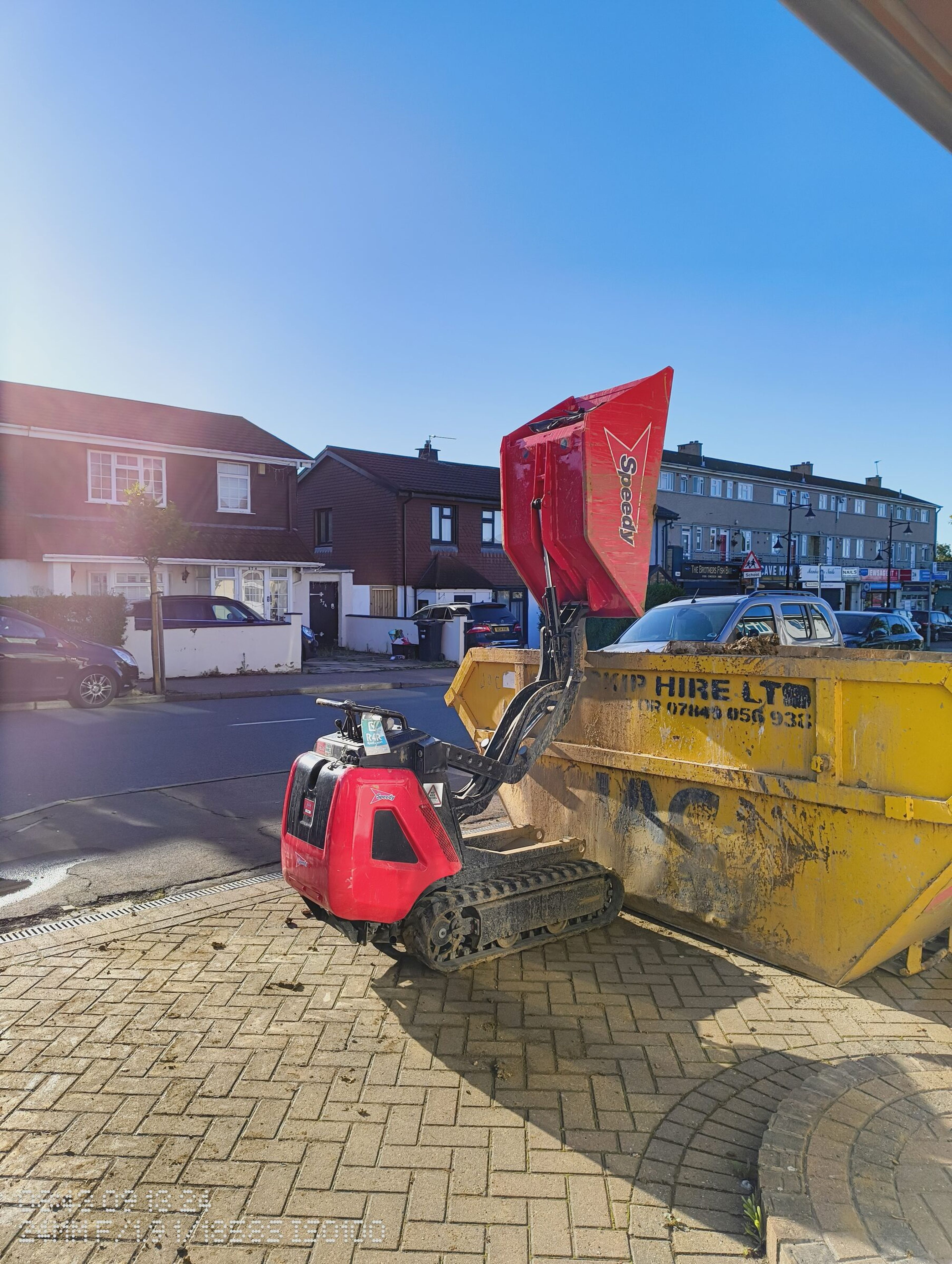 Tracked dumper tipping excavated soil into a skip outside a Chigwell rear extension site.