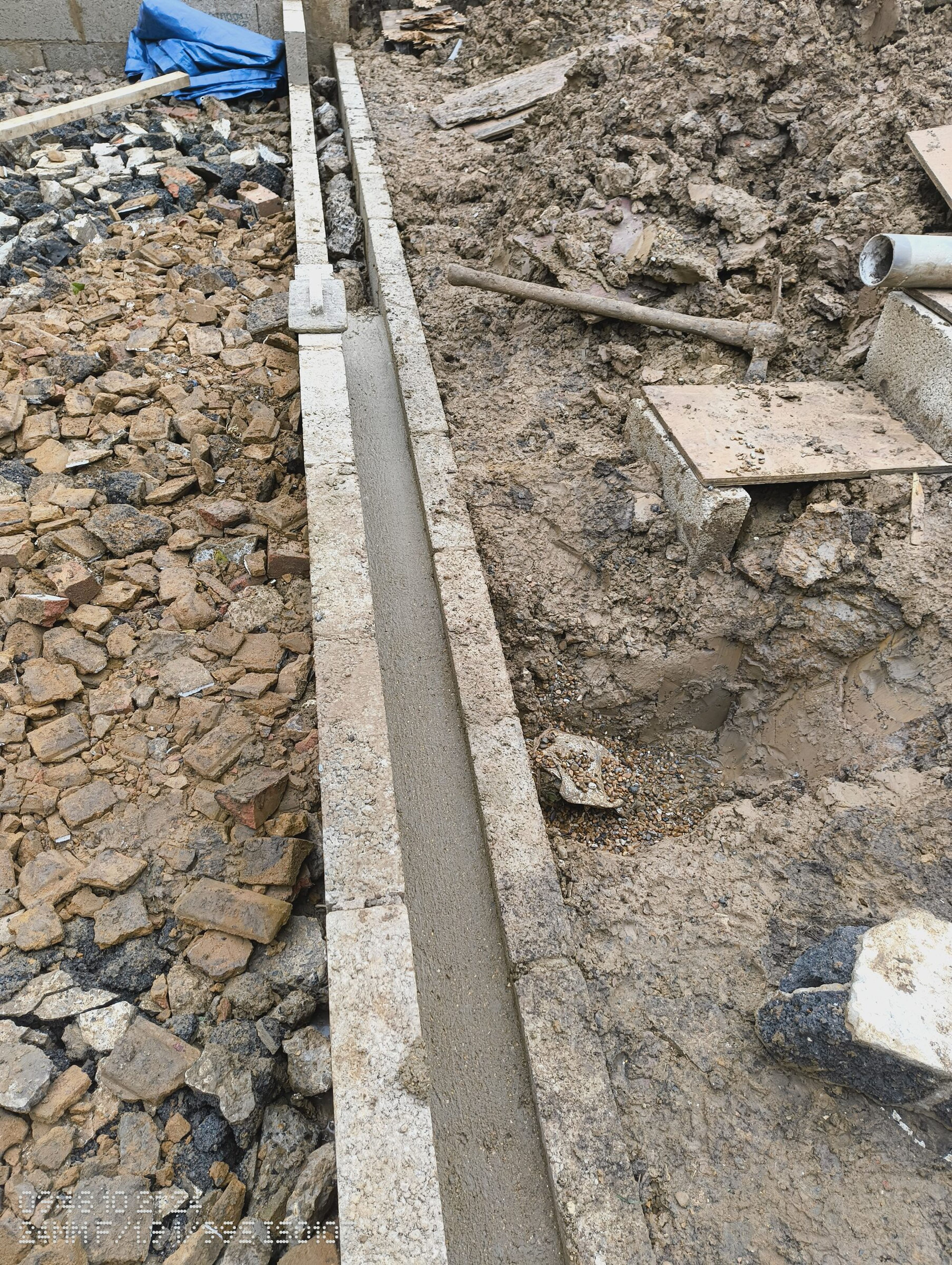 Concrete poured in the shuttered trench beside a run of hardcore.