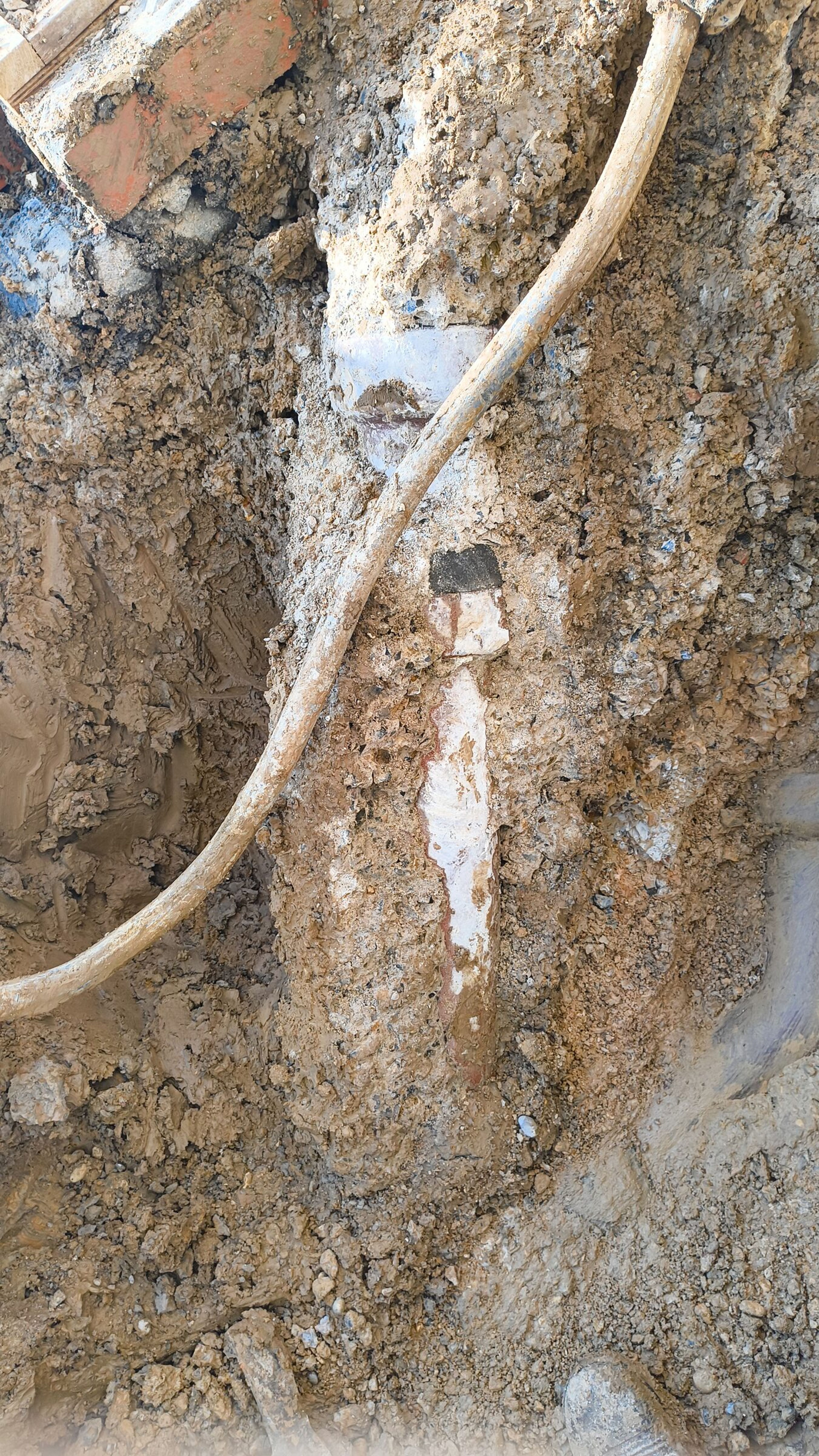 Cable crossing the clay face of the excavation, with brickwork at the top of the trench.