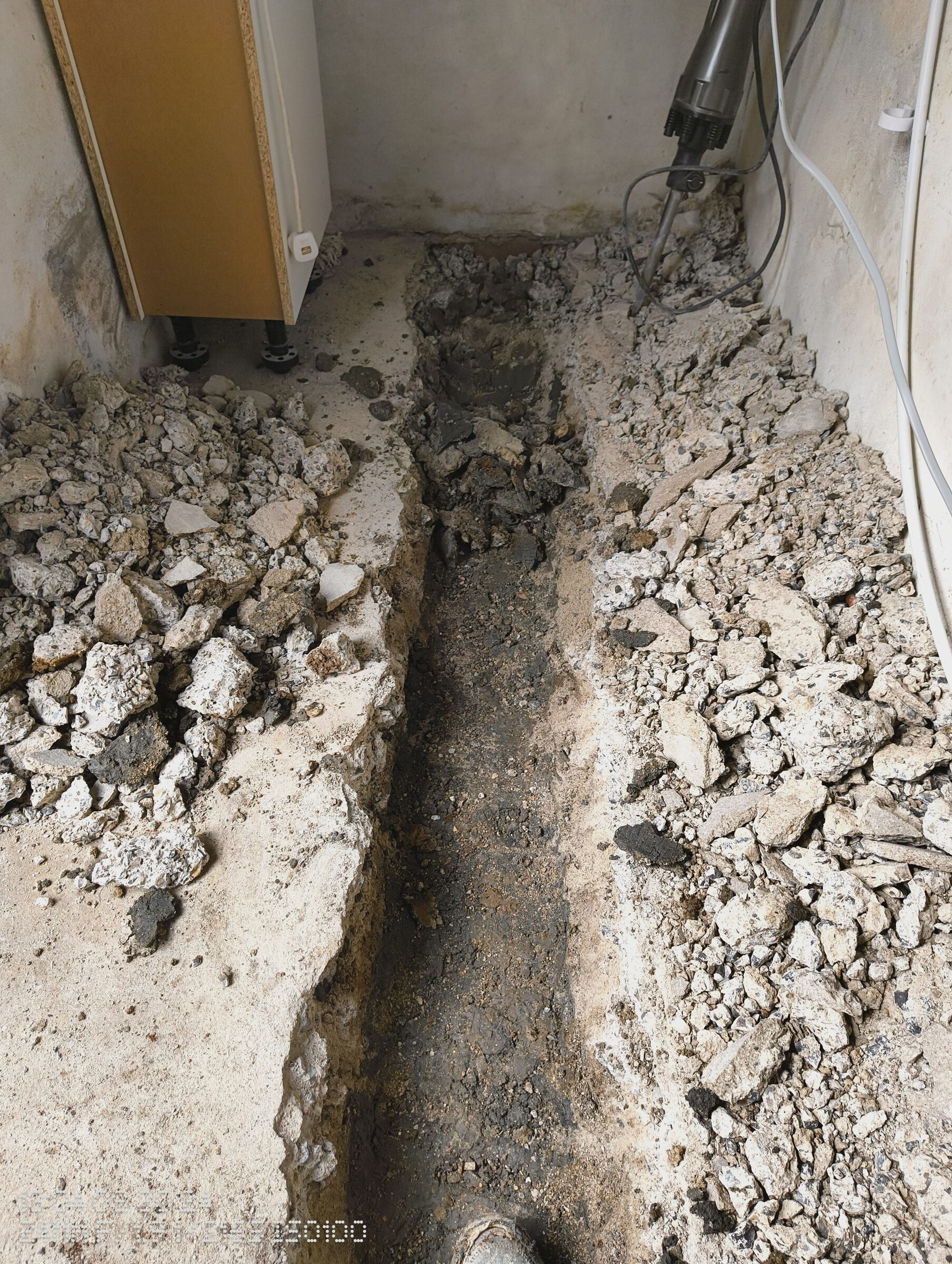 Channel cut through the concrete floor inside, with broken concrete piled either side and a breaker at the far end.