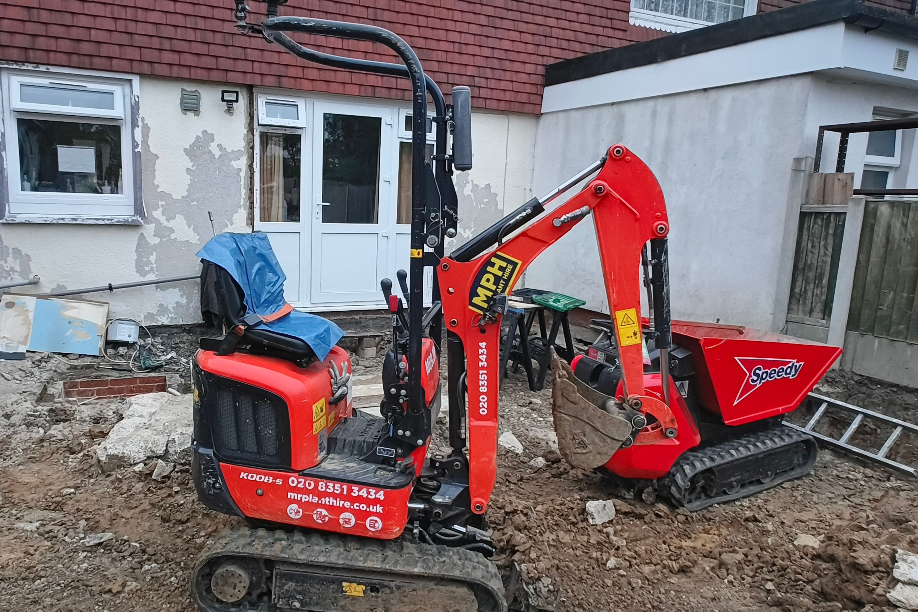 Mini digger and tracked dumper excavating a rear garden during demolition and groundworks for a house extension in Chigwell.