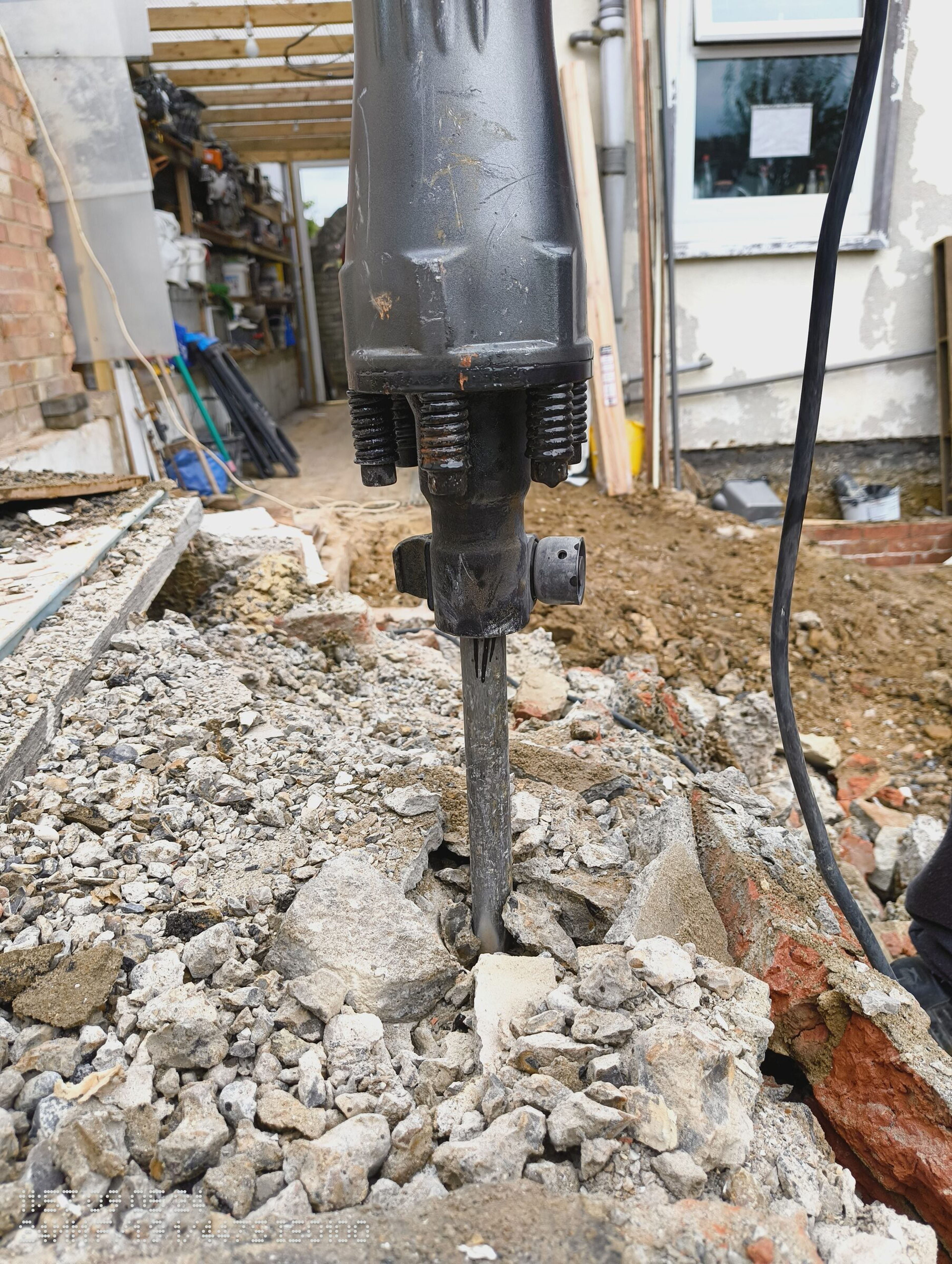 Excavator breaker splitting the concrete and brick rubble from the demolished rear extension.