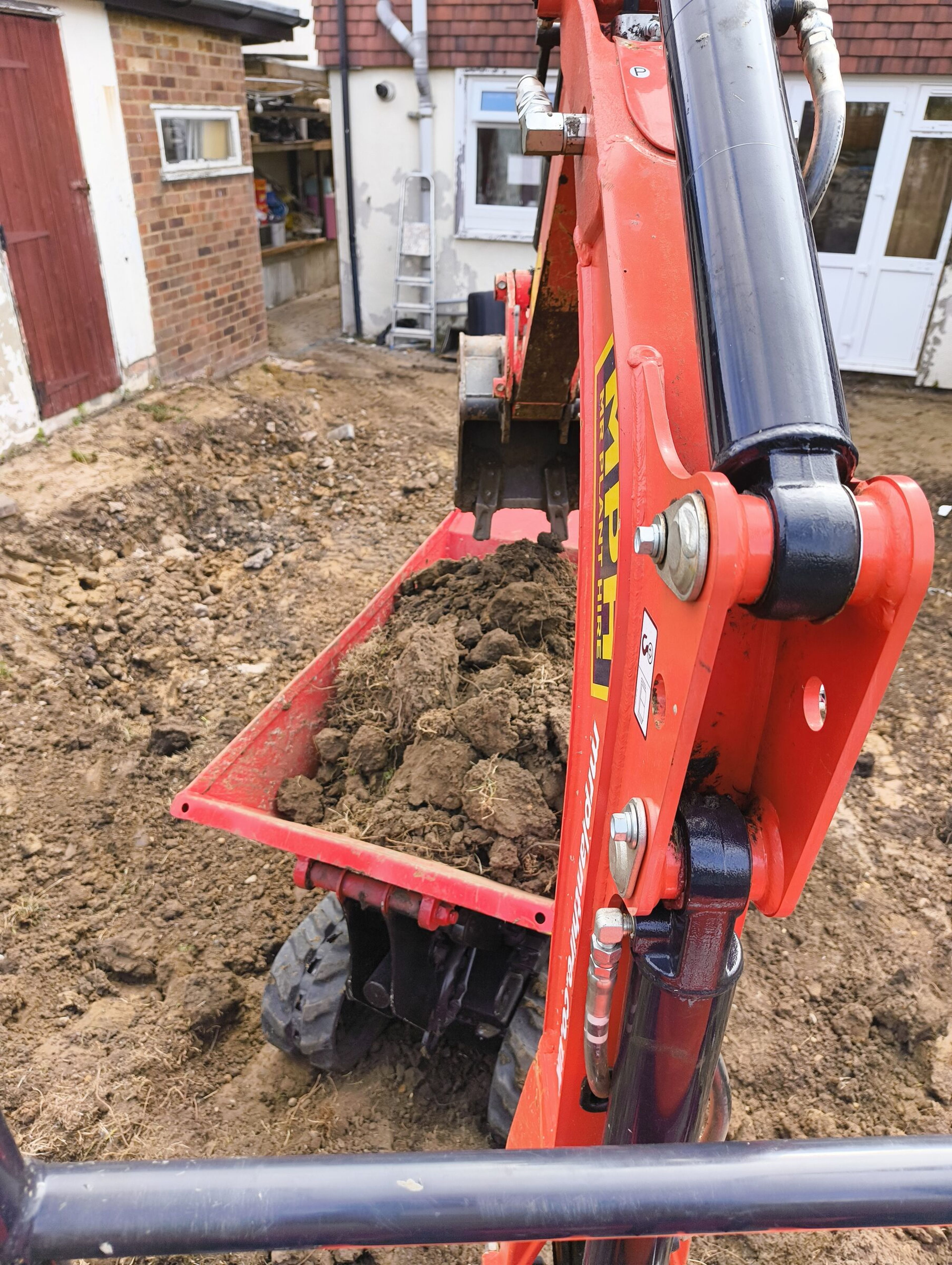 Mini digger loading soil into a tracked dumper for a Chigwell rear extension.