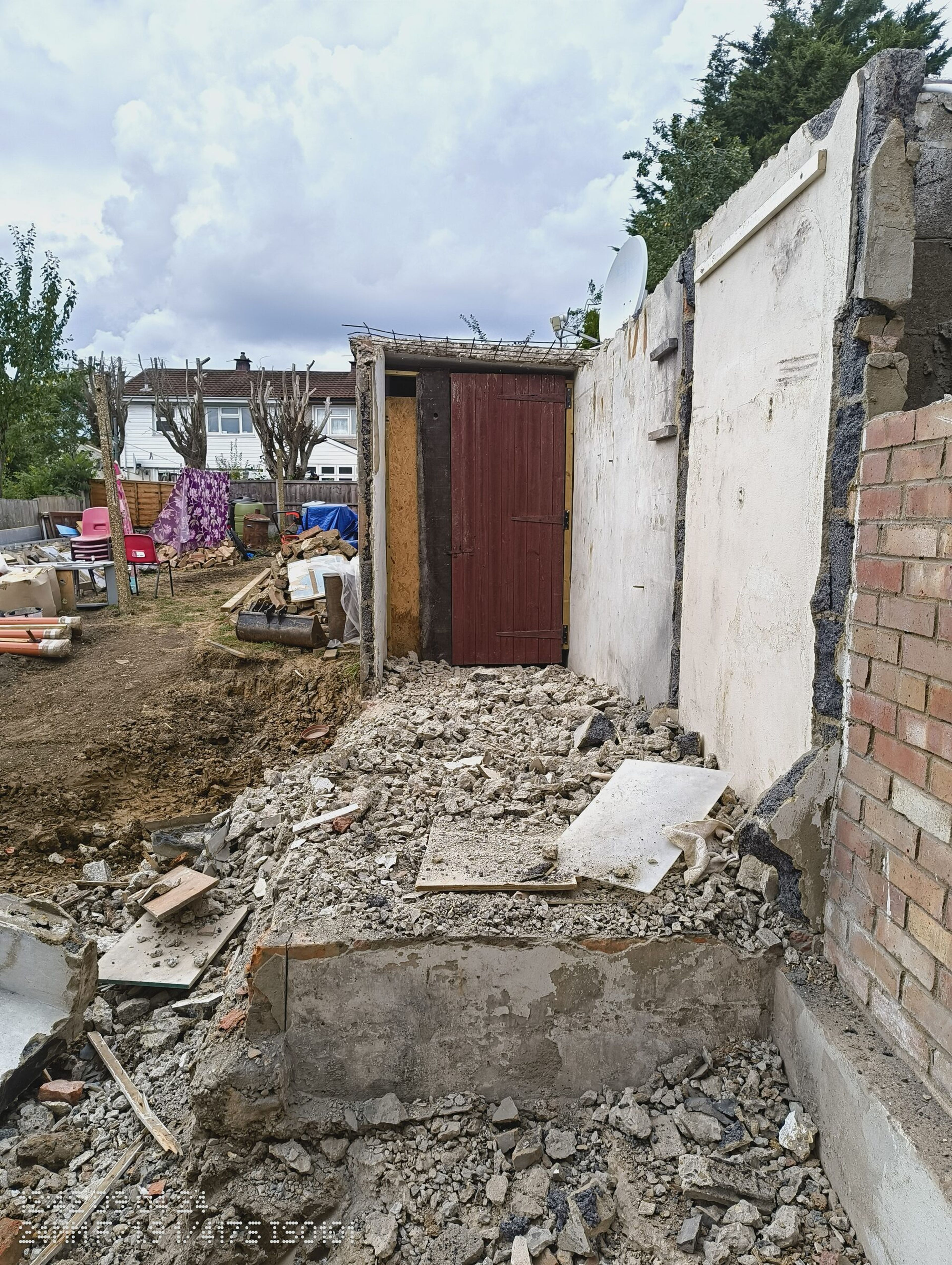 Rubble from the demolished extension, with a remaining rendered wall and red door at the back of the garden.