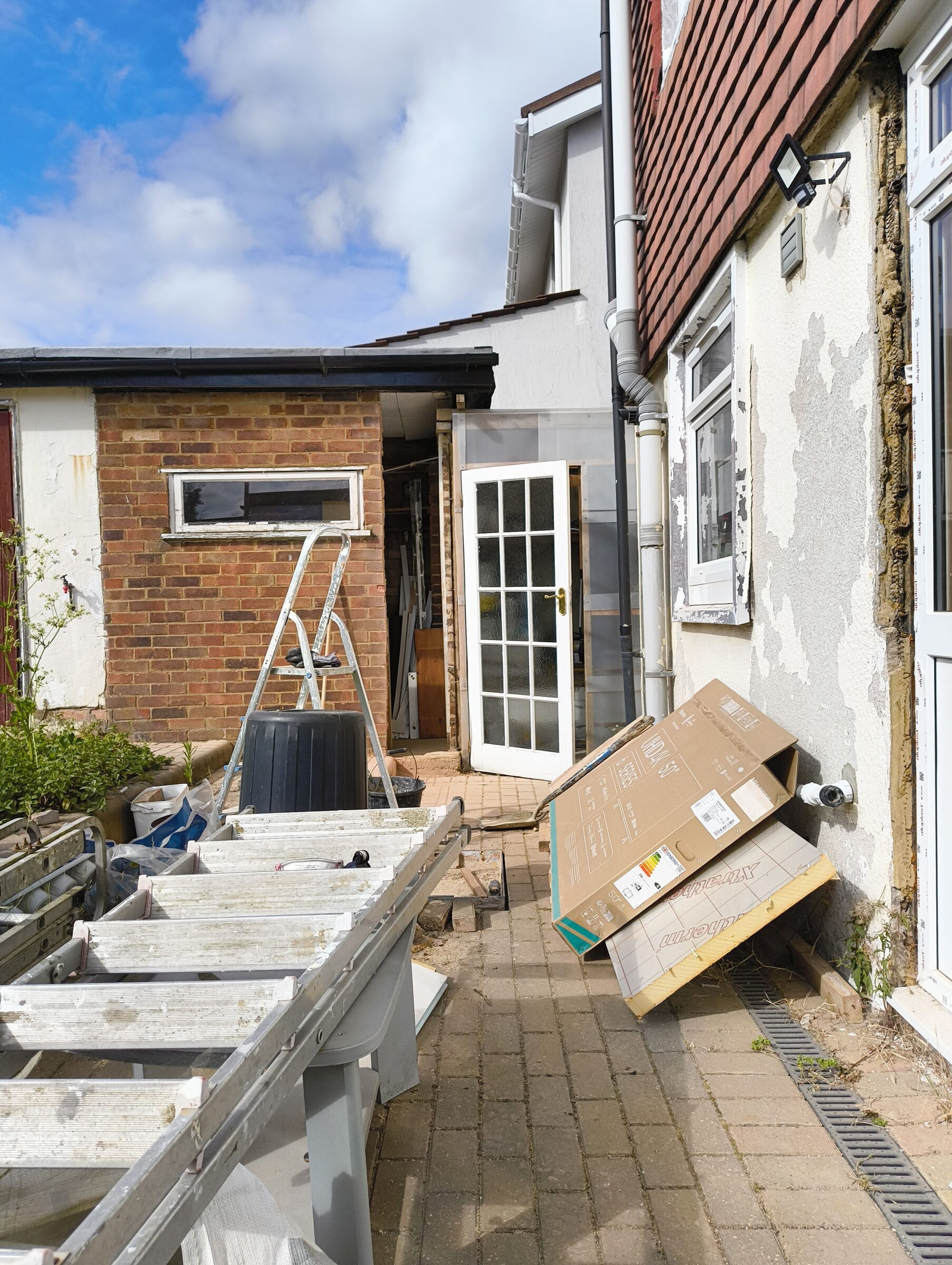 Side passage beside the house during demolition, with ladders, the brick extension, and render taken off the house wall.