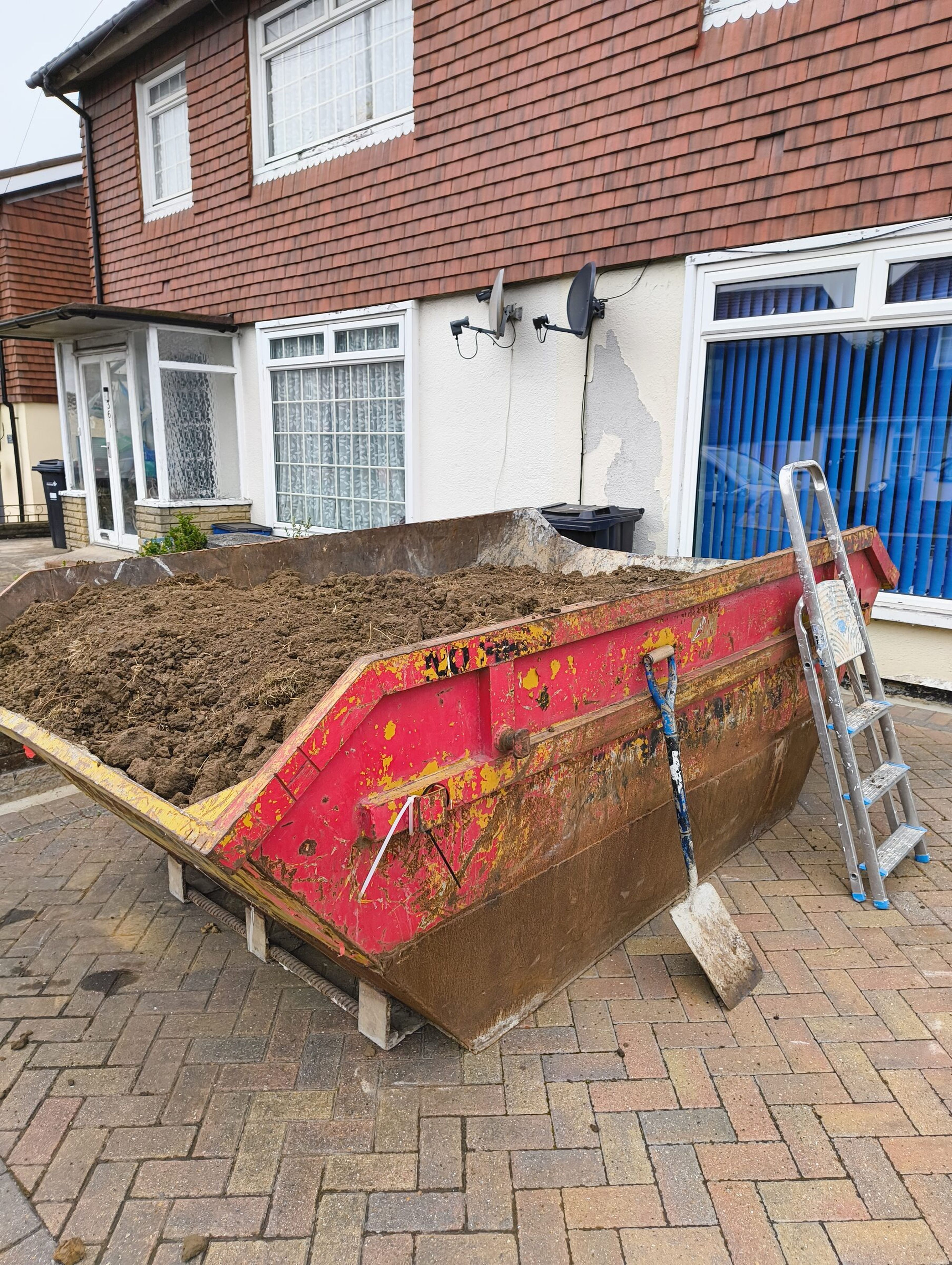 Skip full of excavated soil with stepladder and shovel on a Chigwell rear extension site.