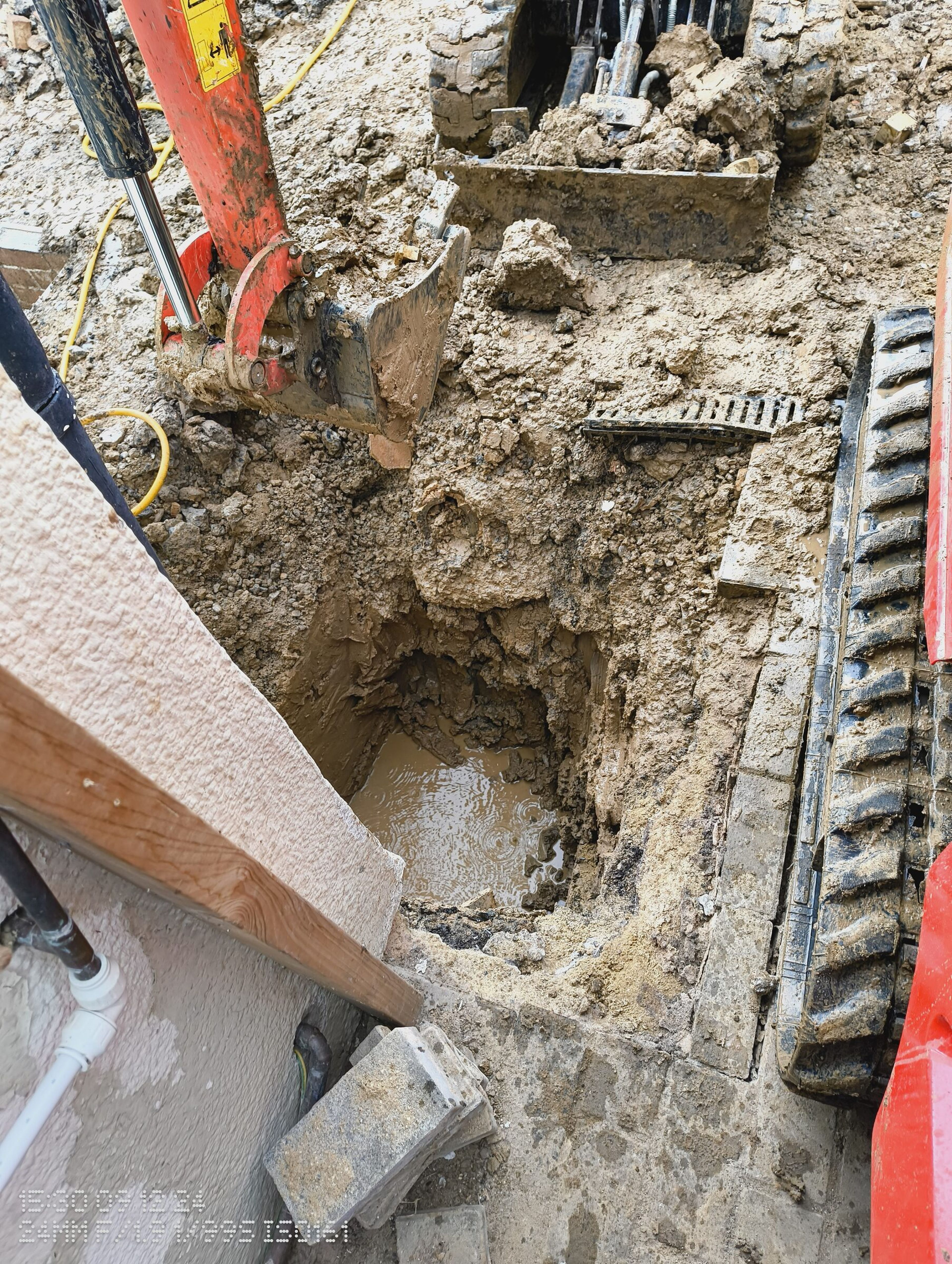Mini digger excavating a deep, water-filled trench beside the house wall for a Chigwell rear extension foundation.