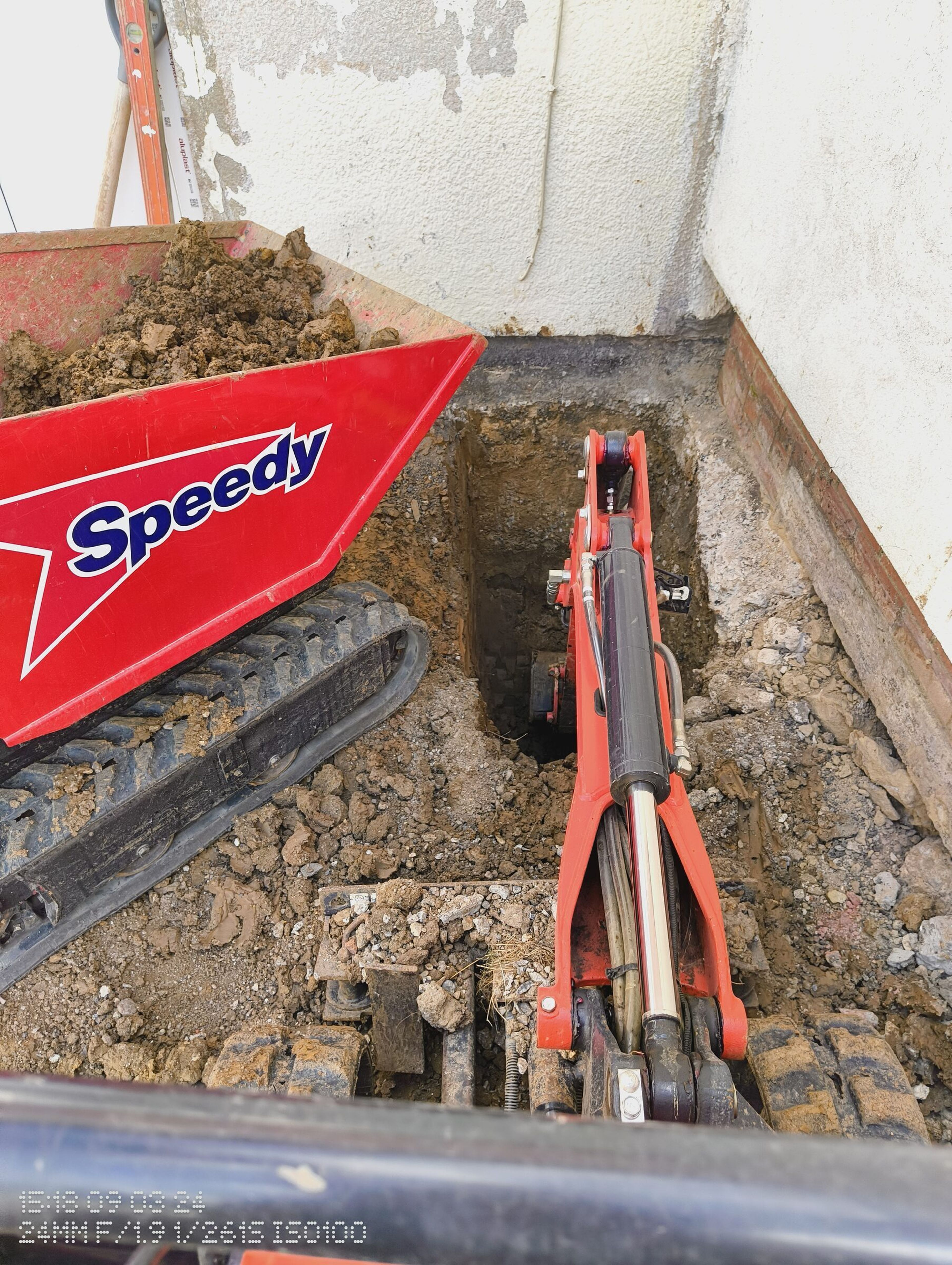 Mini digger and tracked dumper excavating a foundation trench tight to the house wall in Chigwell.