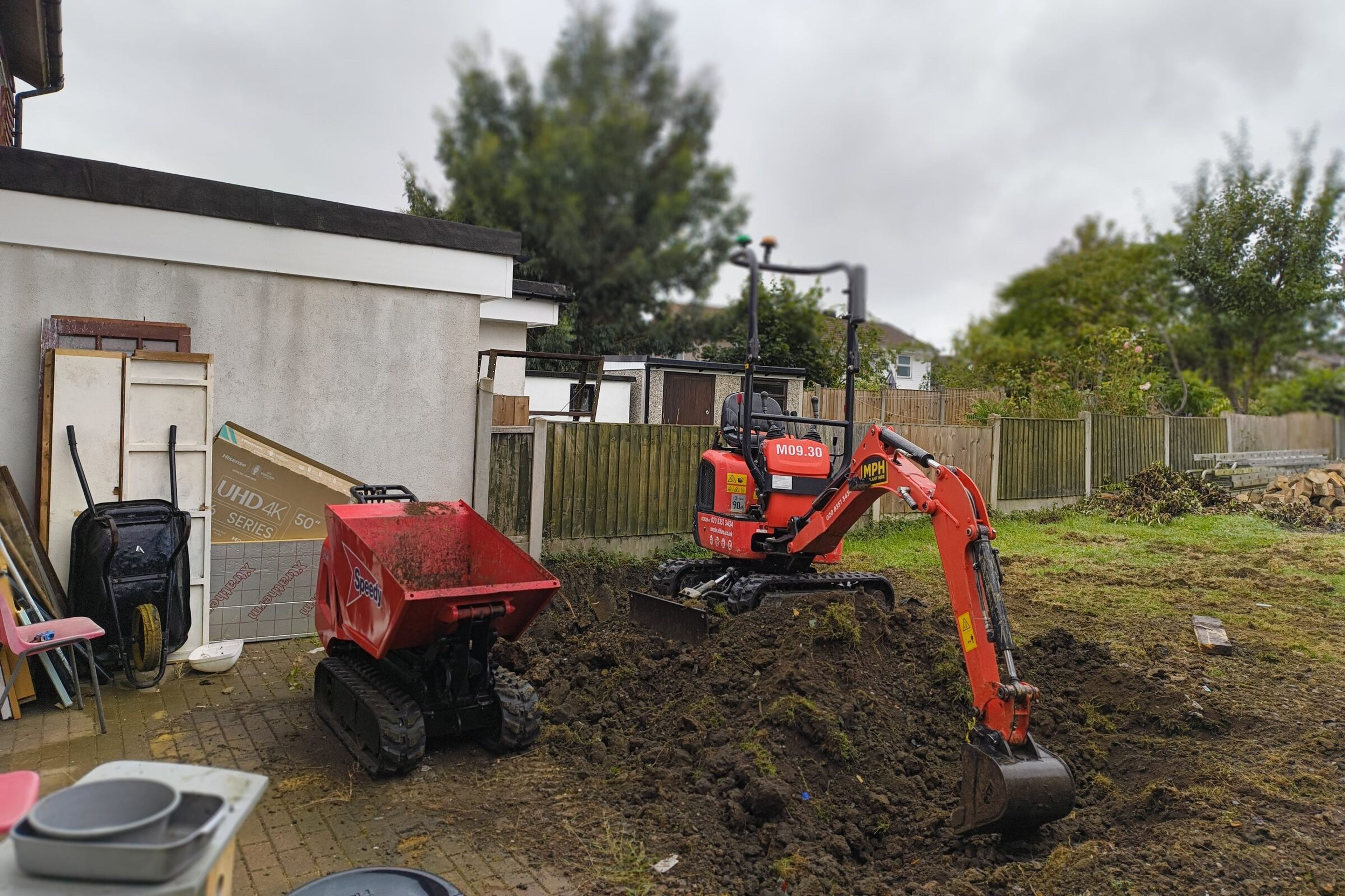 Mini digger and mini tracked dumper excavating a rear garden during demolition and groundworks for a rear house extension in Chigwell.
