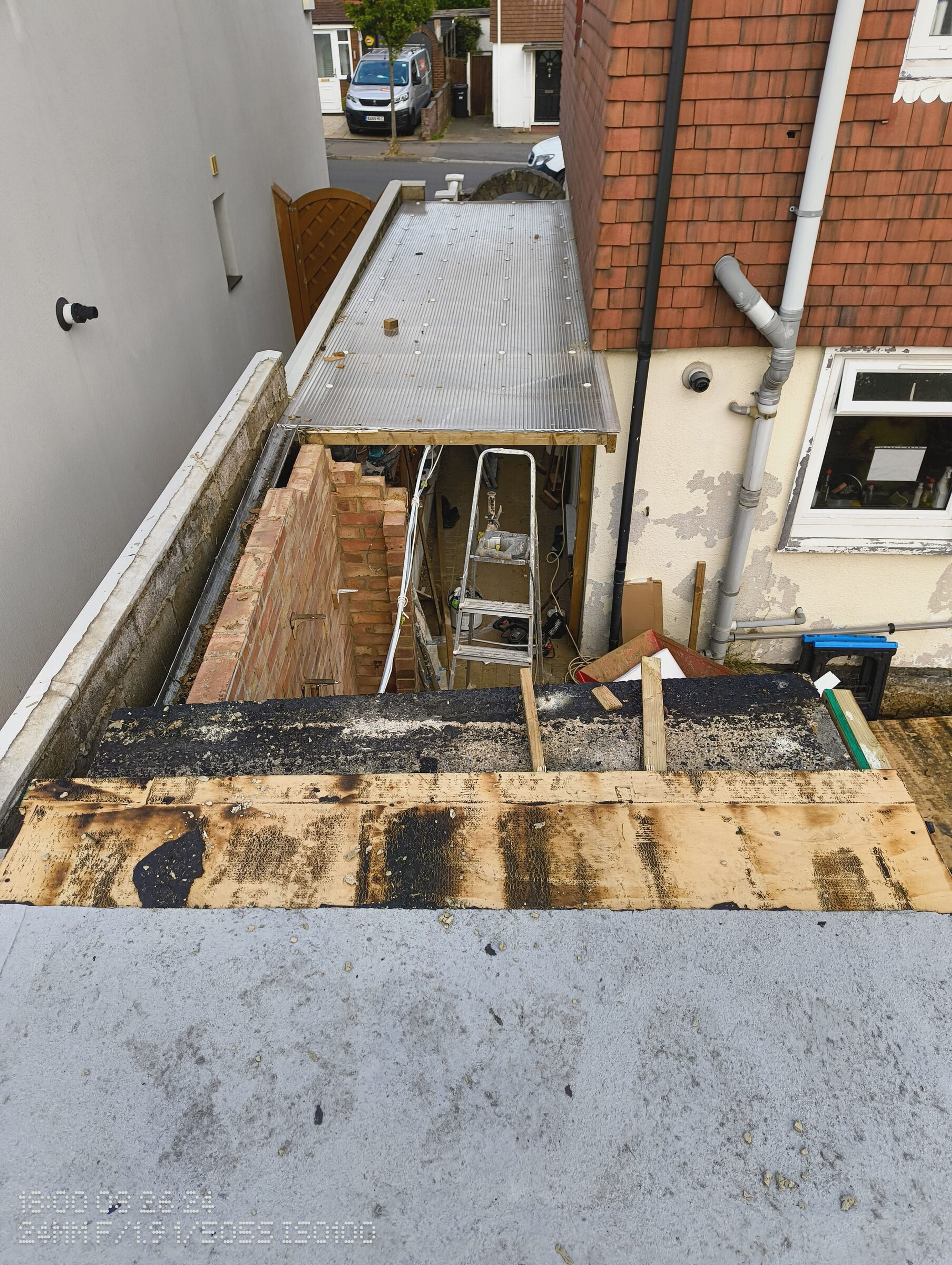Section of the flat roof removed, looking down into the side passage where a stepladder stands under the remaining roof.