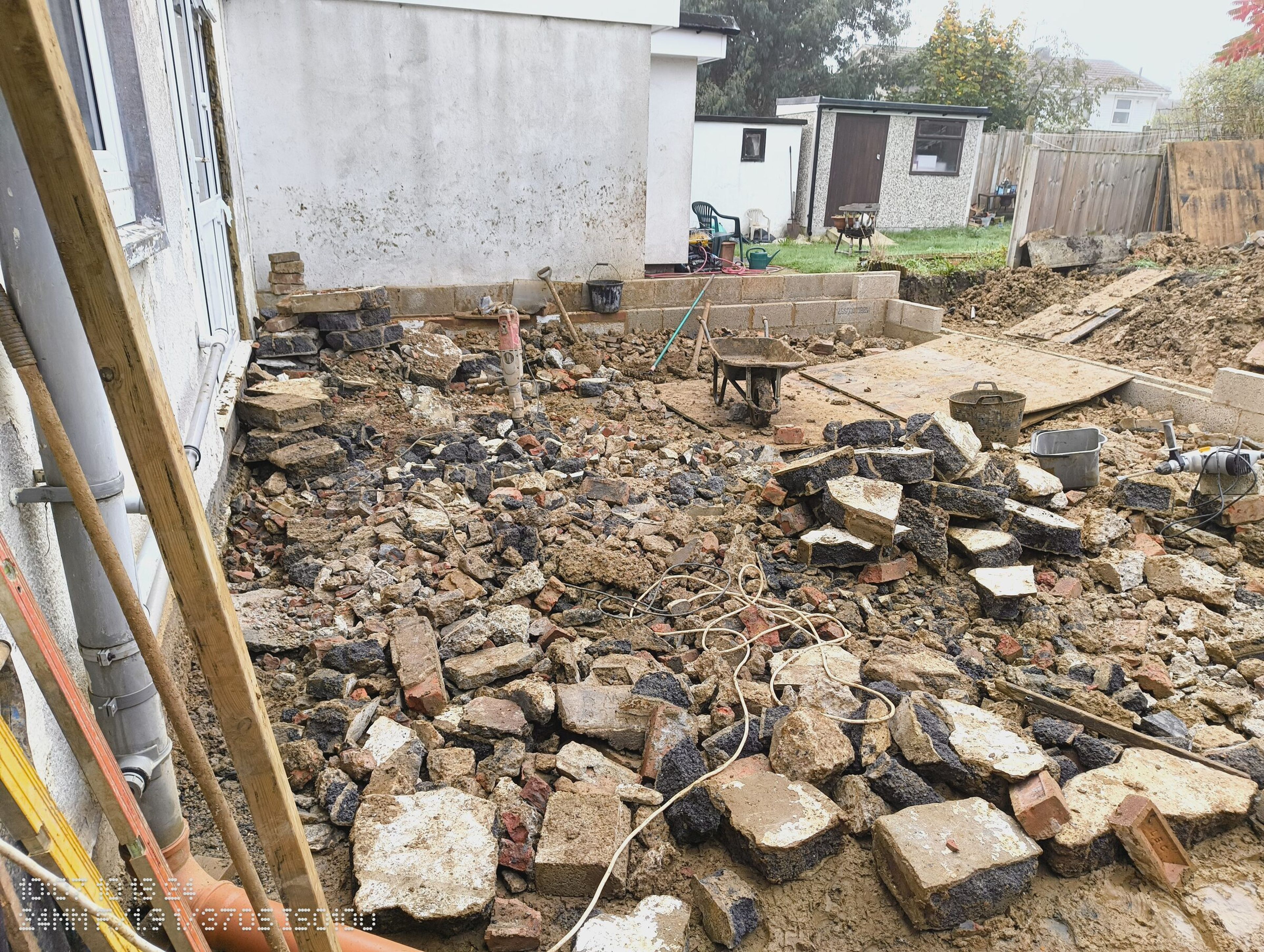Rubble and broken concrete inside the rear extension footprint, with the garden and sheds beyond.