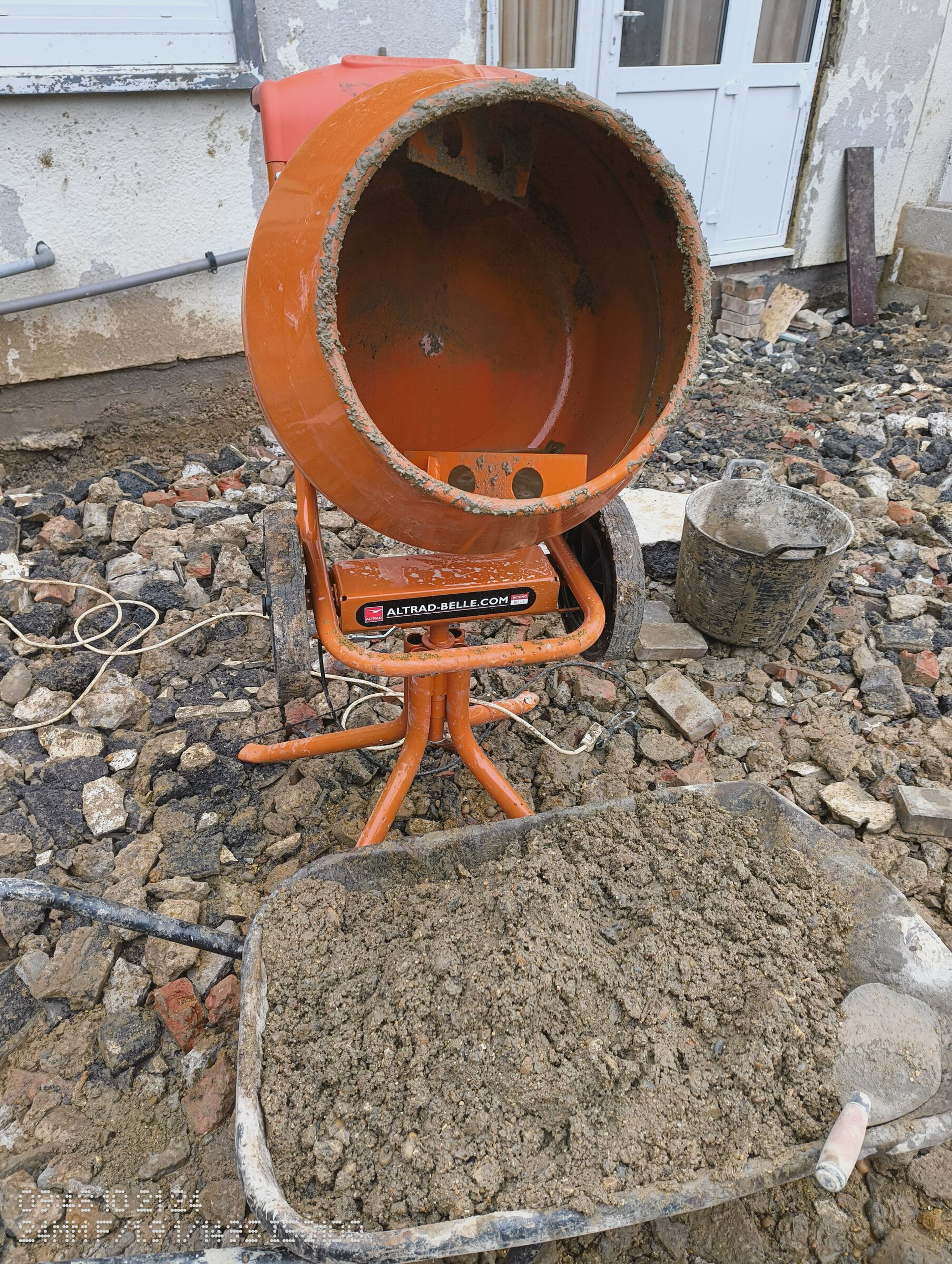 Cement mixer and a wheelbarrow of mixed concrete beside the patio doors.