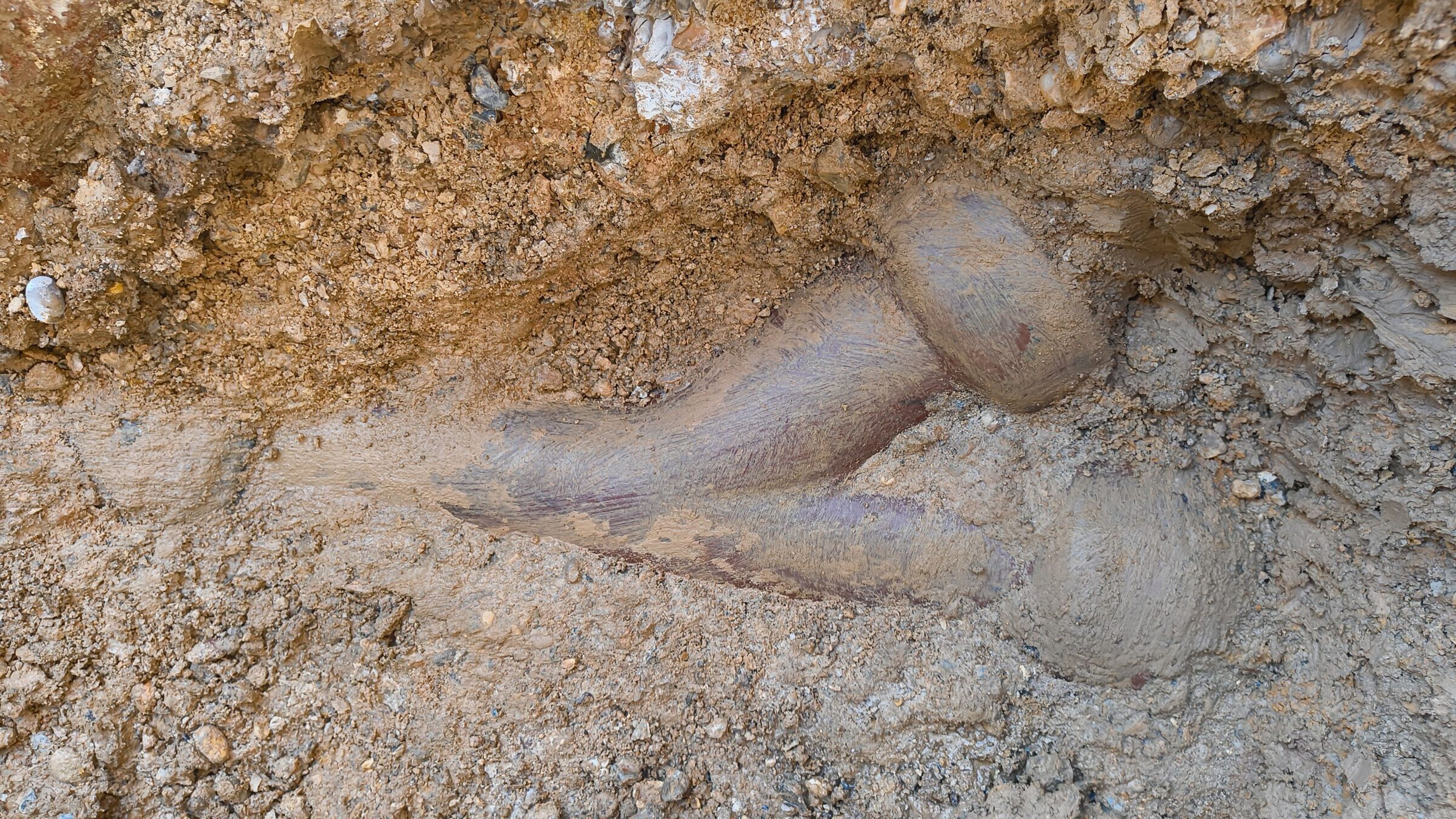 Old pipe bend partly uncovered in the clay face of the trench.