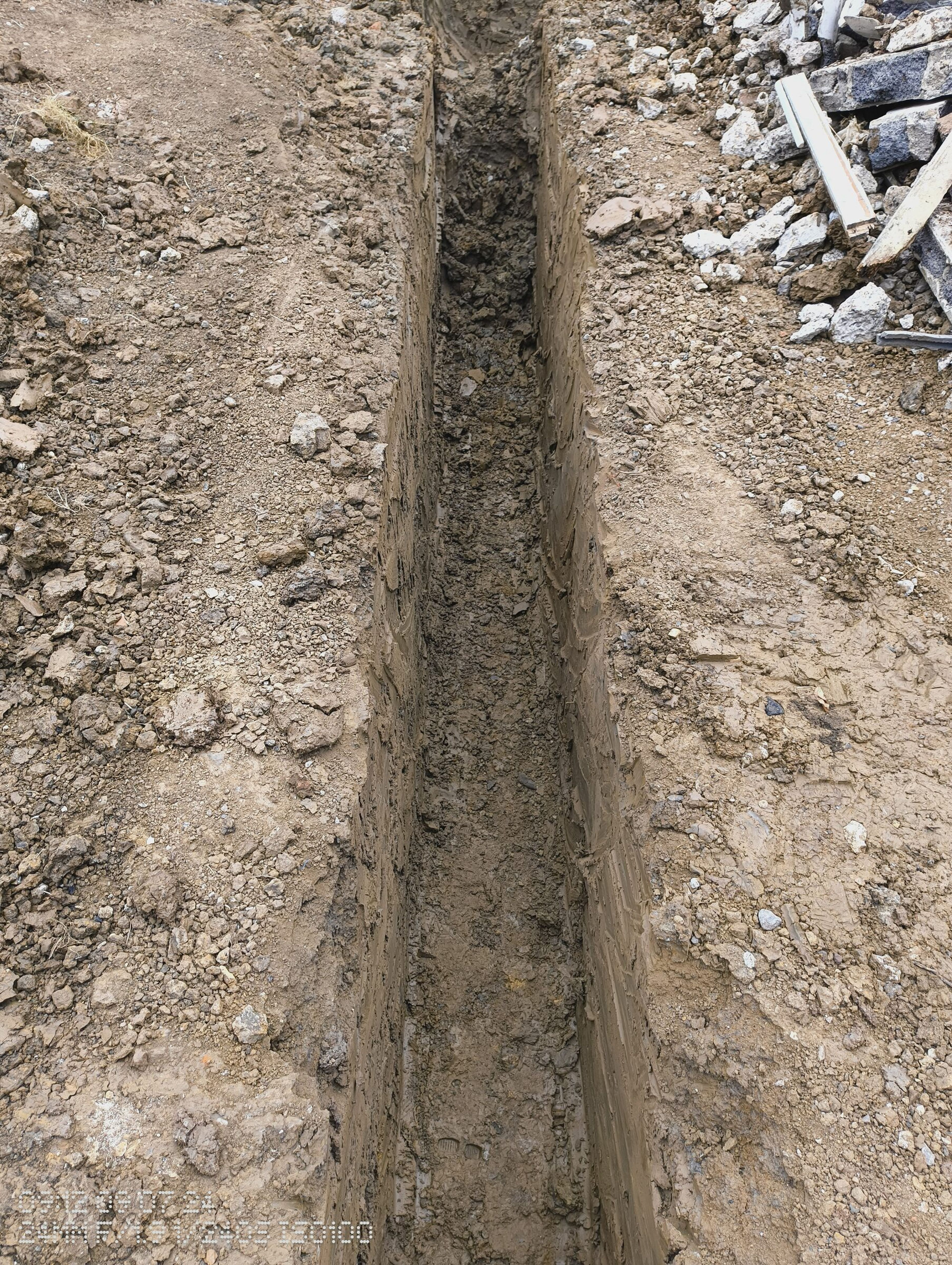 Narrow foundation trench dug through clay soil for a rear extension in Chigwell, with broken concrete piled alongside.