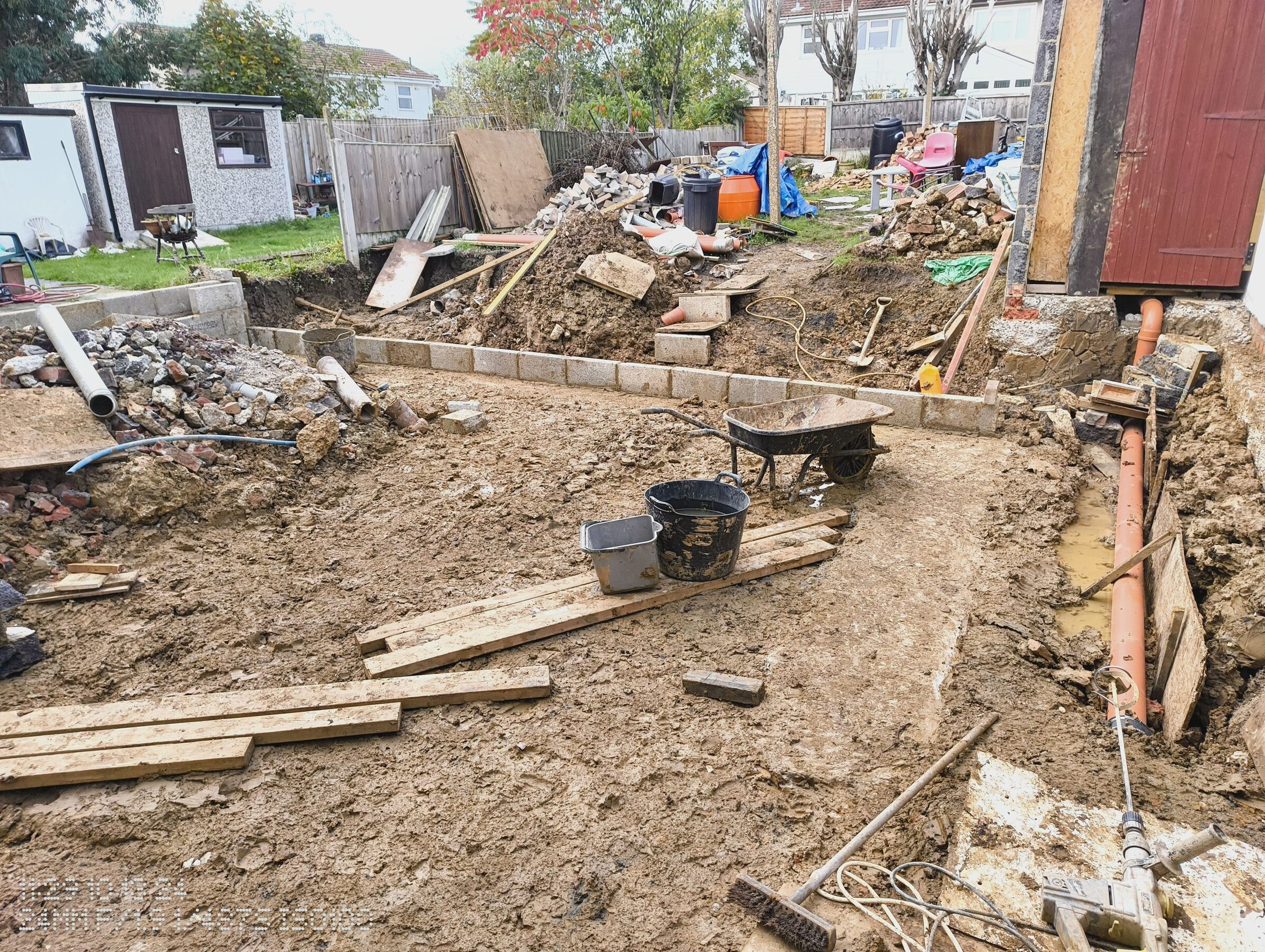 Low block wall around the footprint, with timber, a wheelbarrow and the garden beyond.