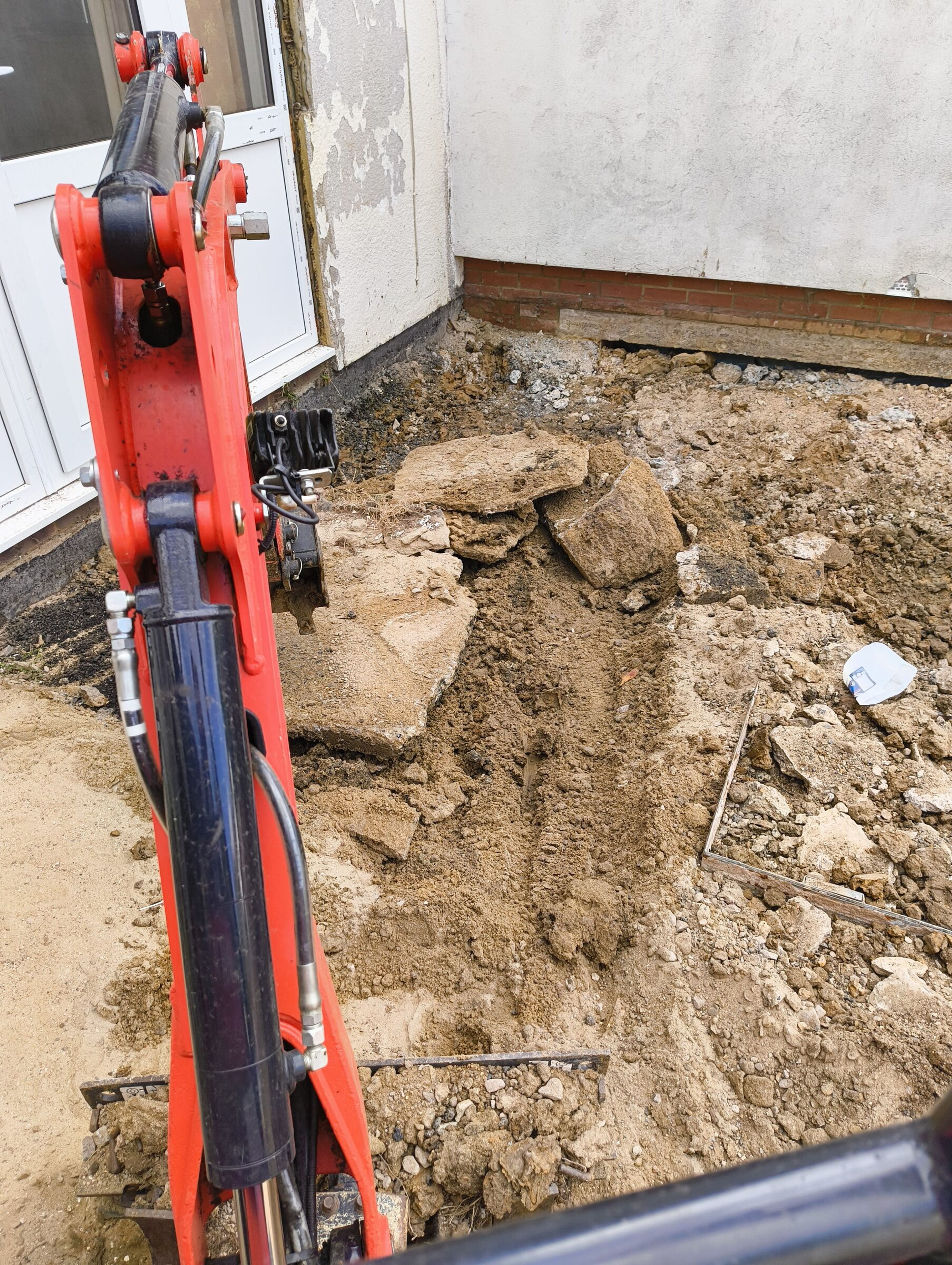 Mini digger moving a large rock while levelling ground for a Chigwell rear extension.