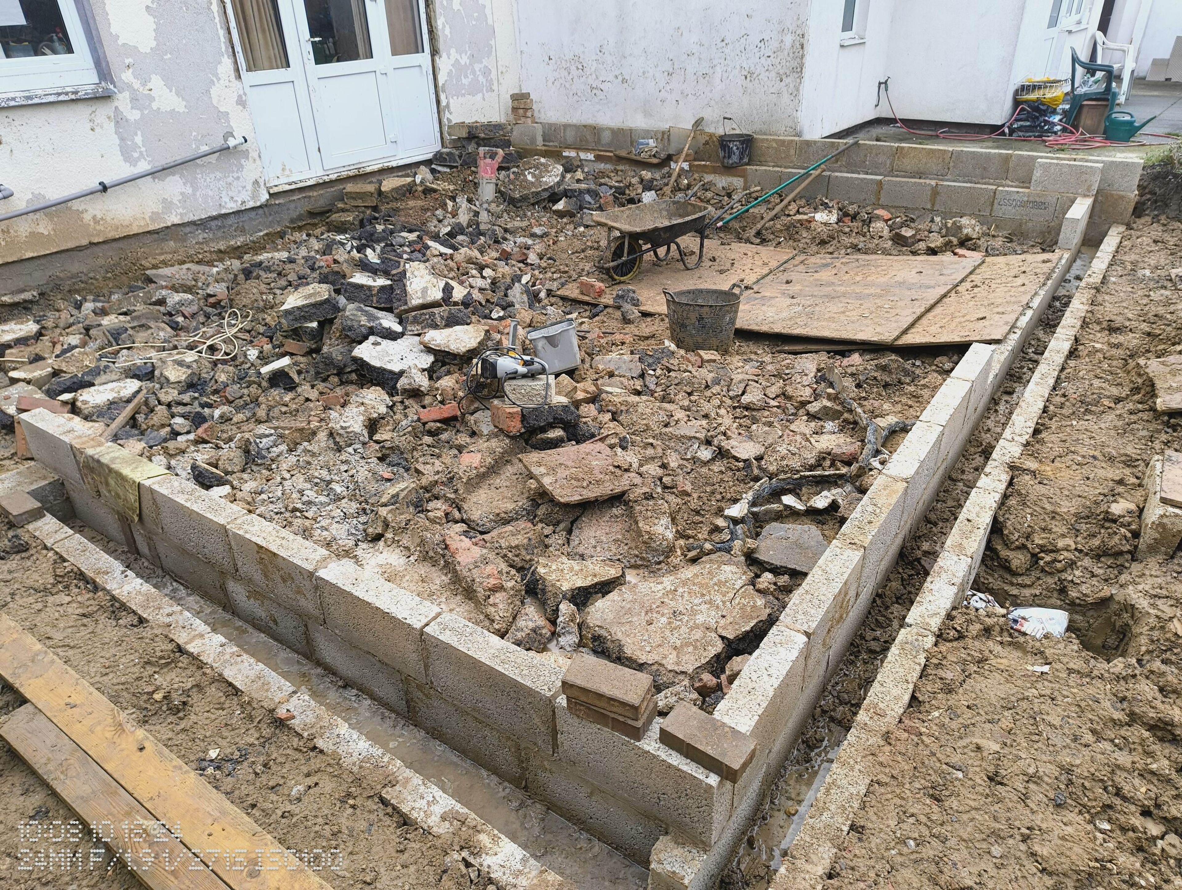 Blockwork walls and timber shuttering around the rubble-filled footprint, in front of the patio doors.