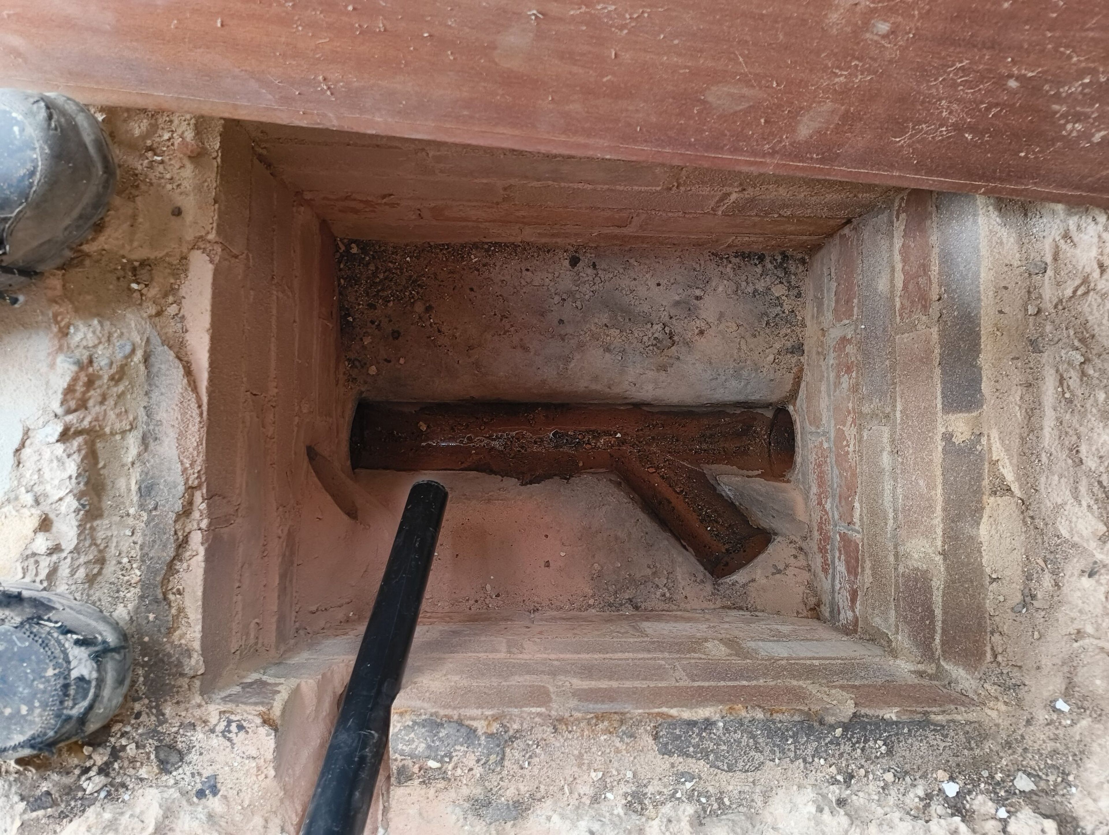 Old pipe junction exposed inside a brick chamber beneath the timber floor.