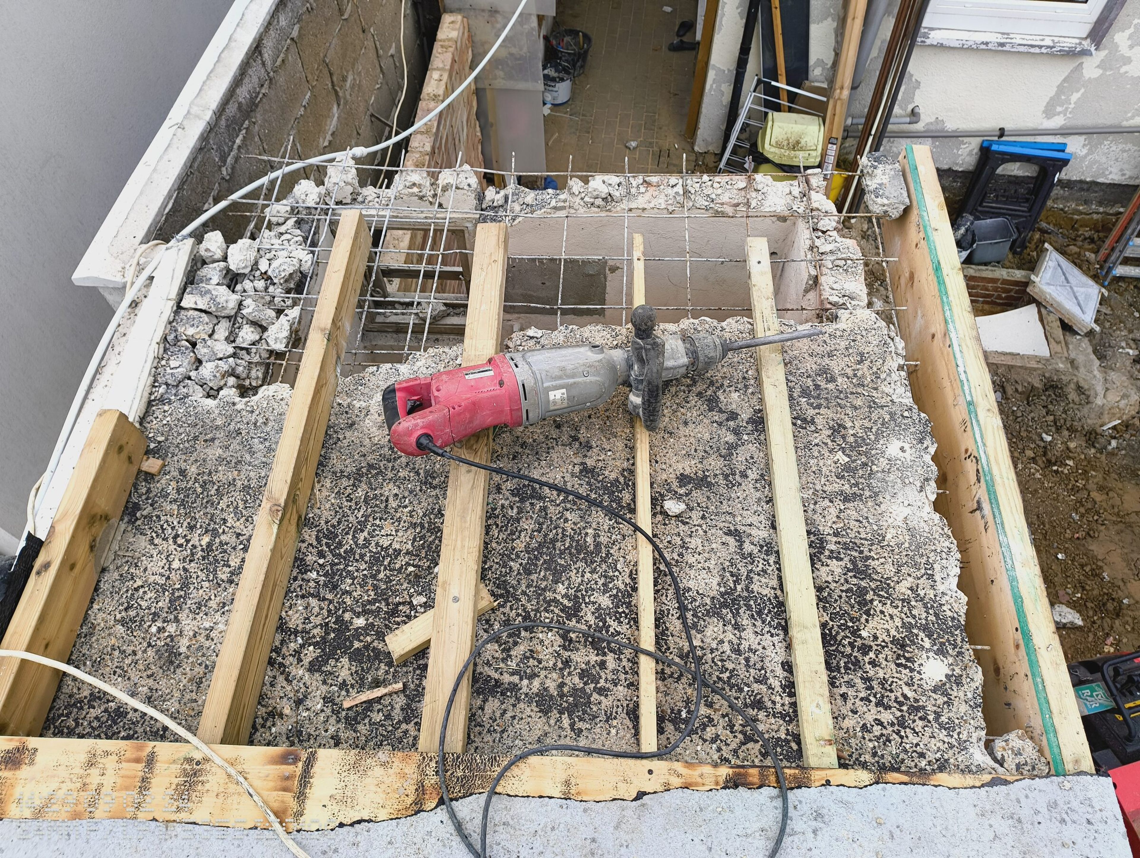 Breaker on the opened concrete roof of the Chigwell rear extension, with timber joists and steel mesh exposed.