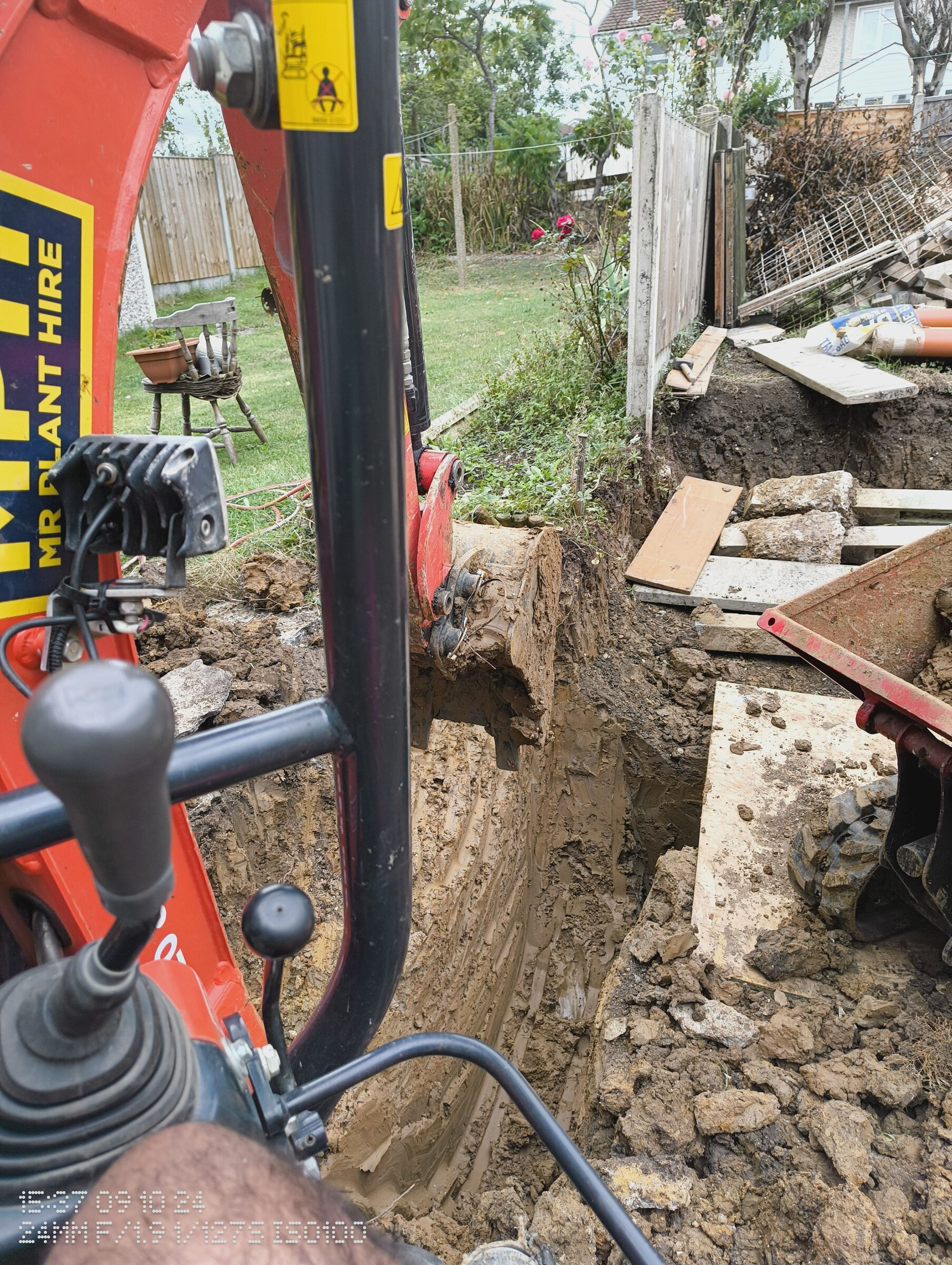 Mini digger bucket digging a deep foundation trench in clay for a rear extension in Chigwell.