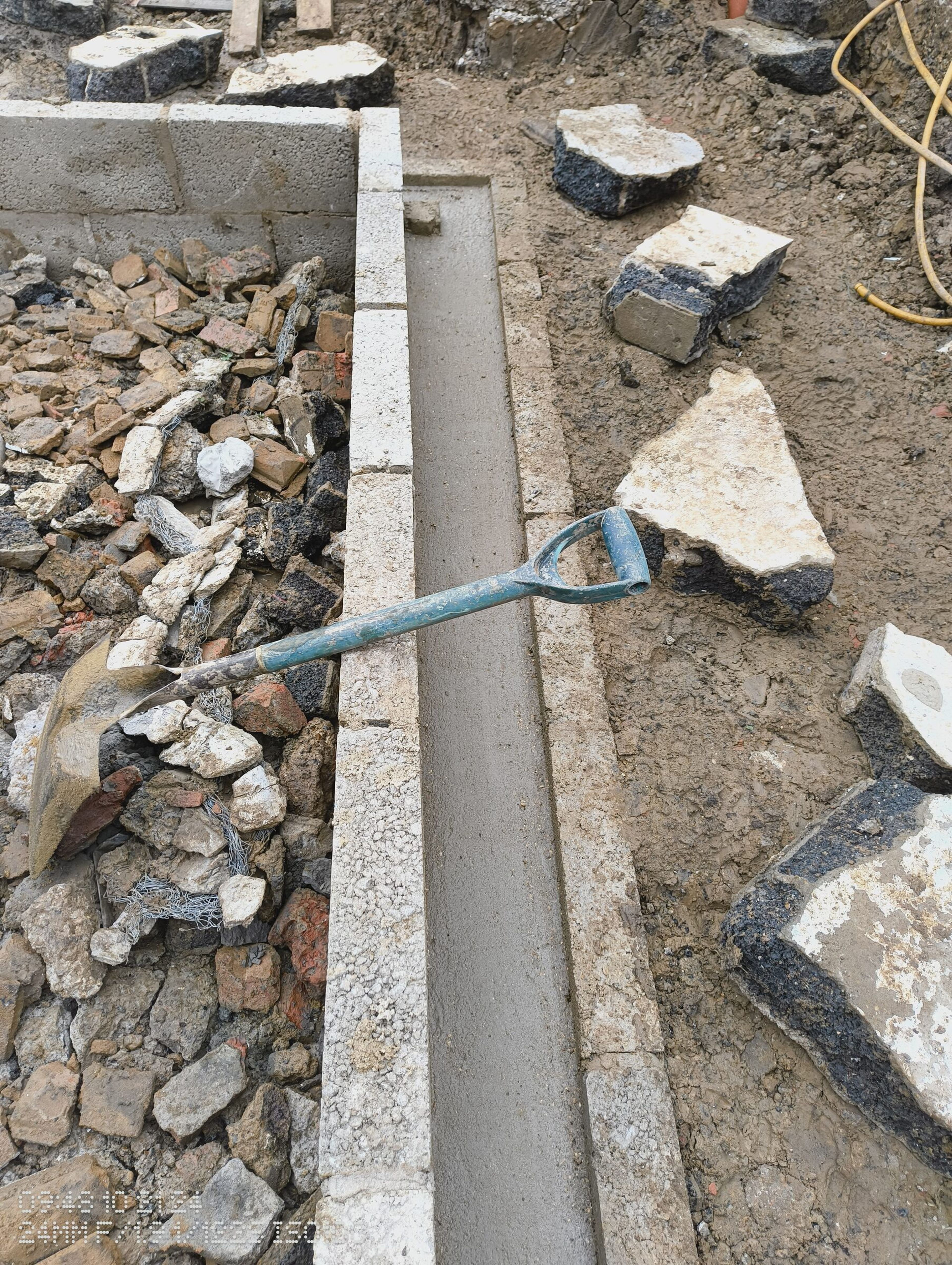 Shovel on the shuttering, with concrete in the trench along the blockwork wall.