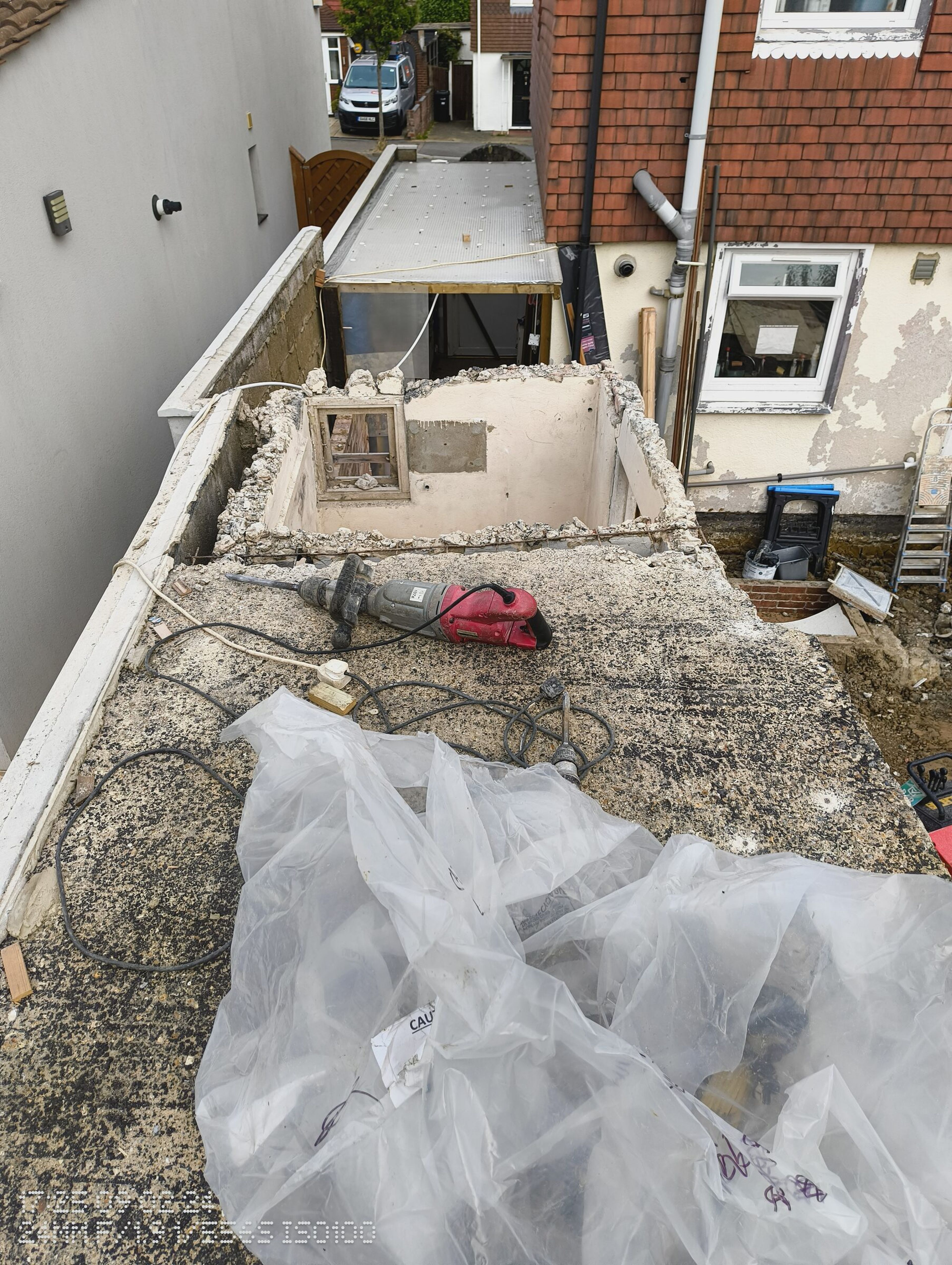 Large opening broken through the extension roof, with a breaker and rubble bags on the remaining slab.