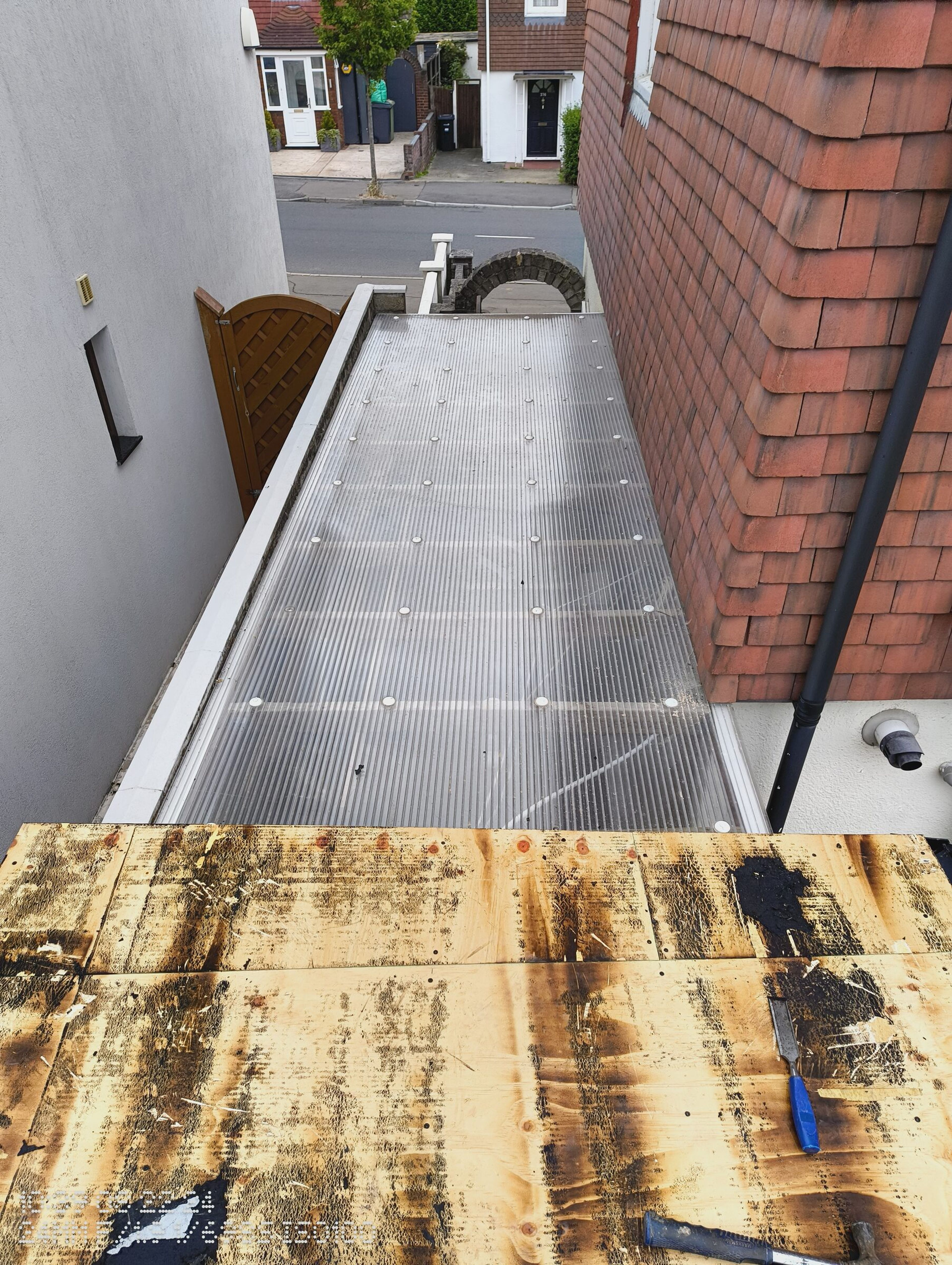 View from the flat roof along the polycarbonate side return towards the street, with the stripped timber deck in front.