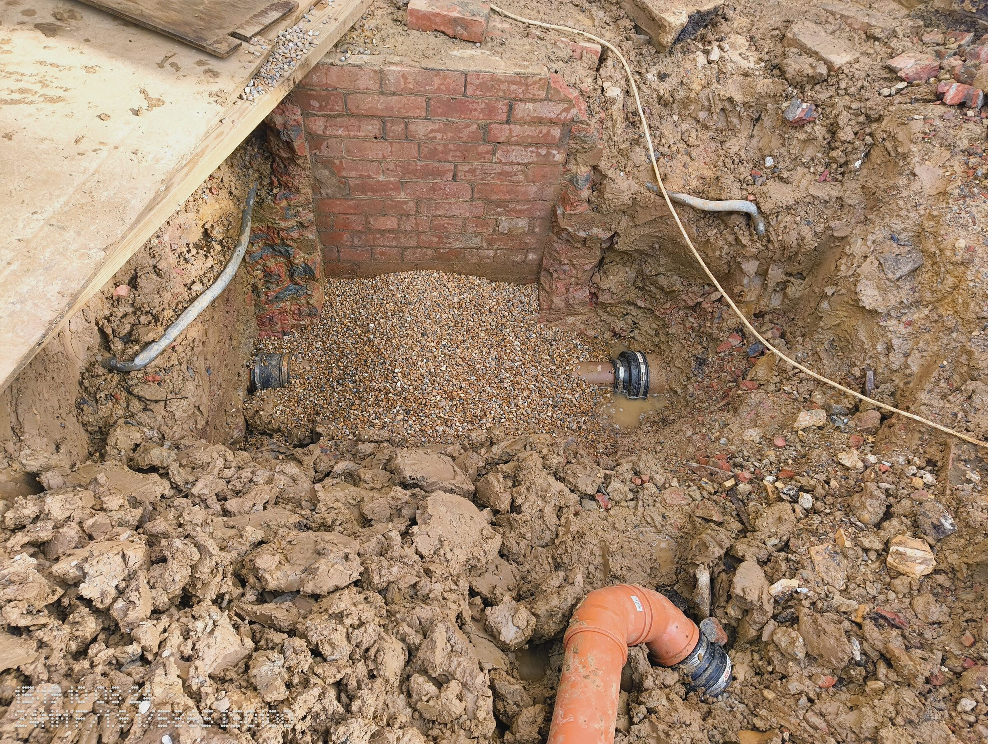 Brick inspection chamber and new orange drainage pipe in a gravel-bedded trench on the Chigwell rear extension.