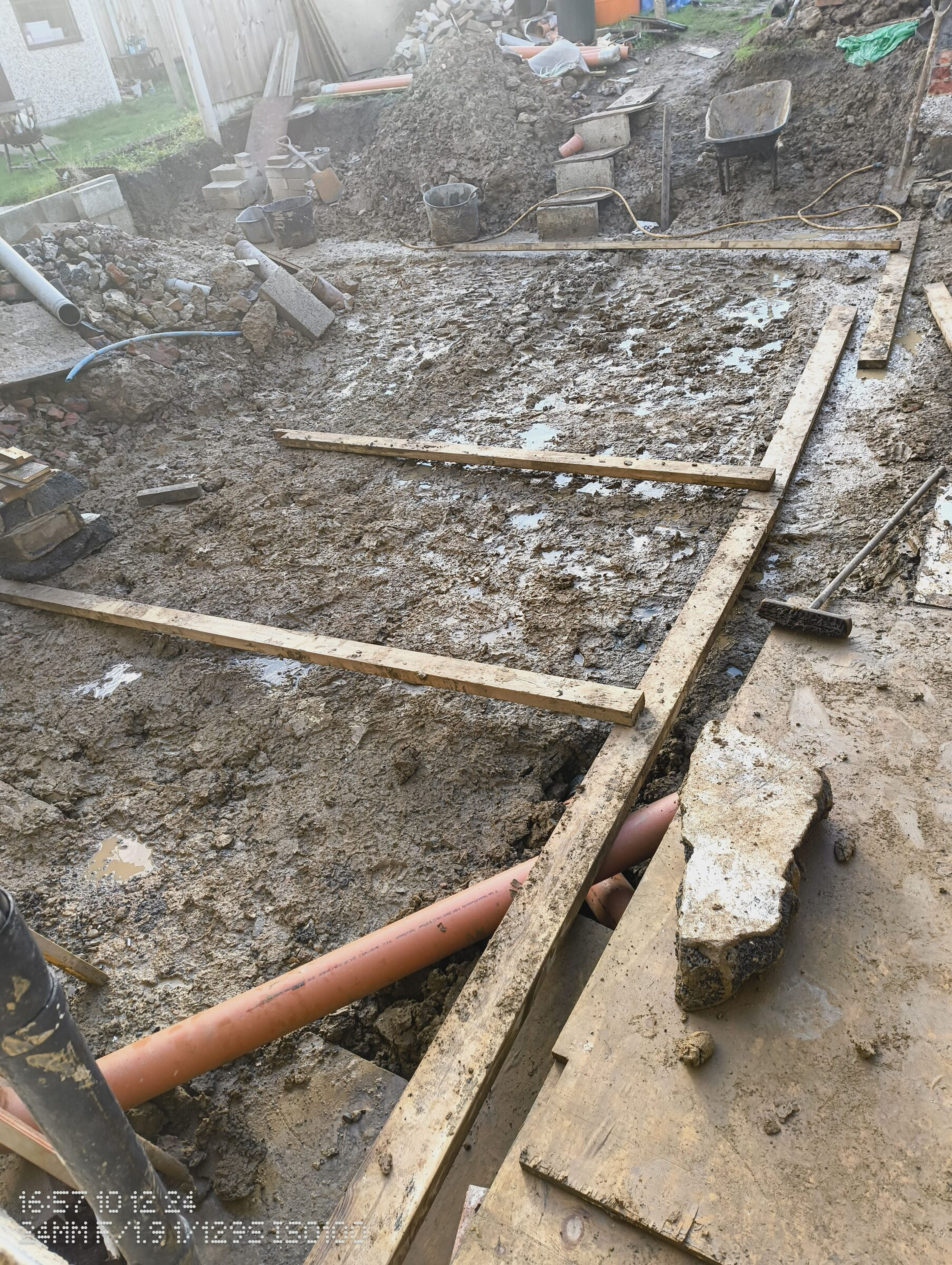 Orange drainage pipe crossing the trench, with timber set out over the dig.