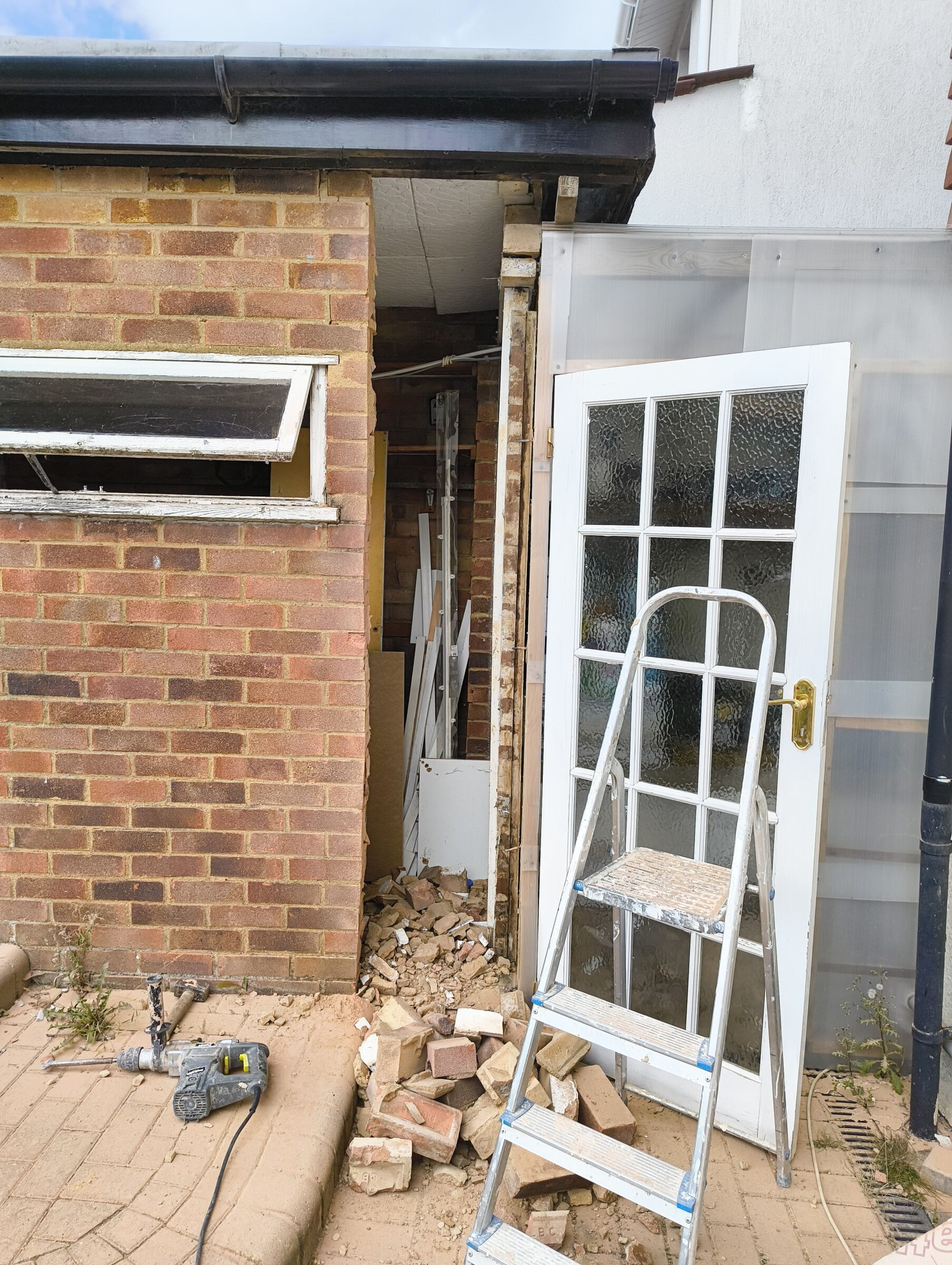 Wider opening broken through the extension wall, with loose bricks by the door and a drill on the patio.