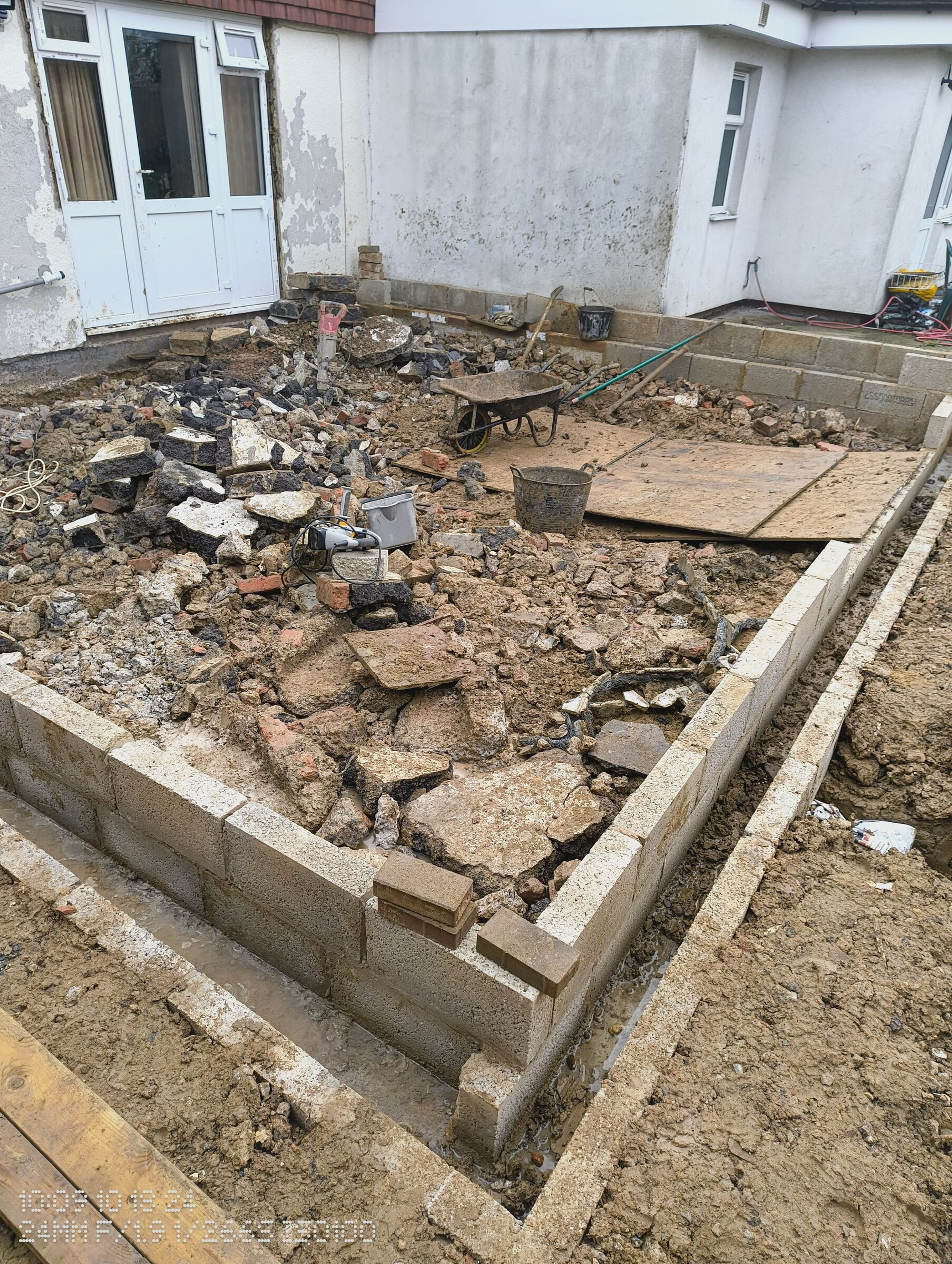 Corner of the new blockwork, shuttered along the outside, with a wheelbarrow on the rubble inside.