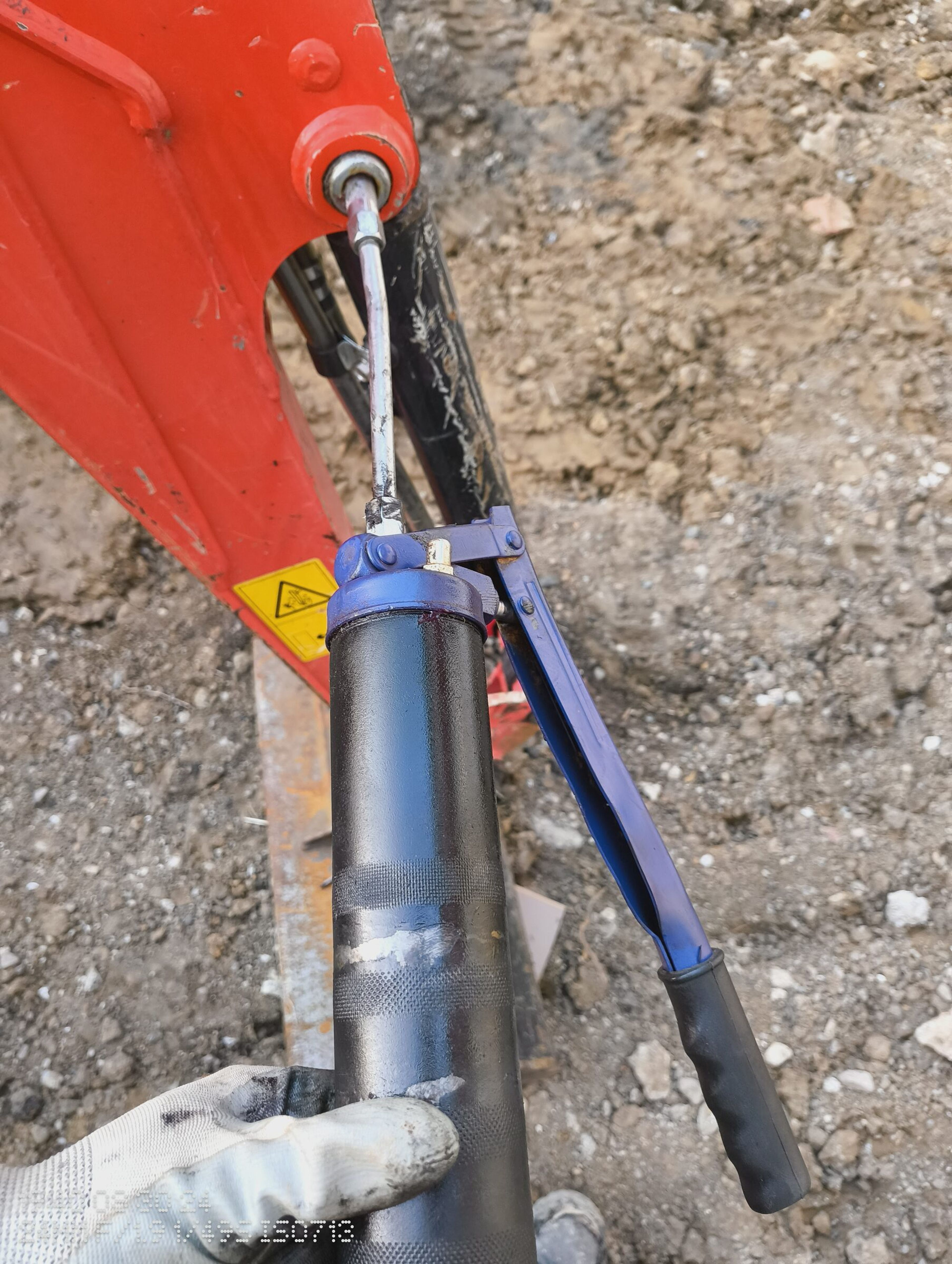 Greasing the mini digger arm during maintenance on a Chigwell rear extension site.