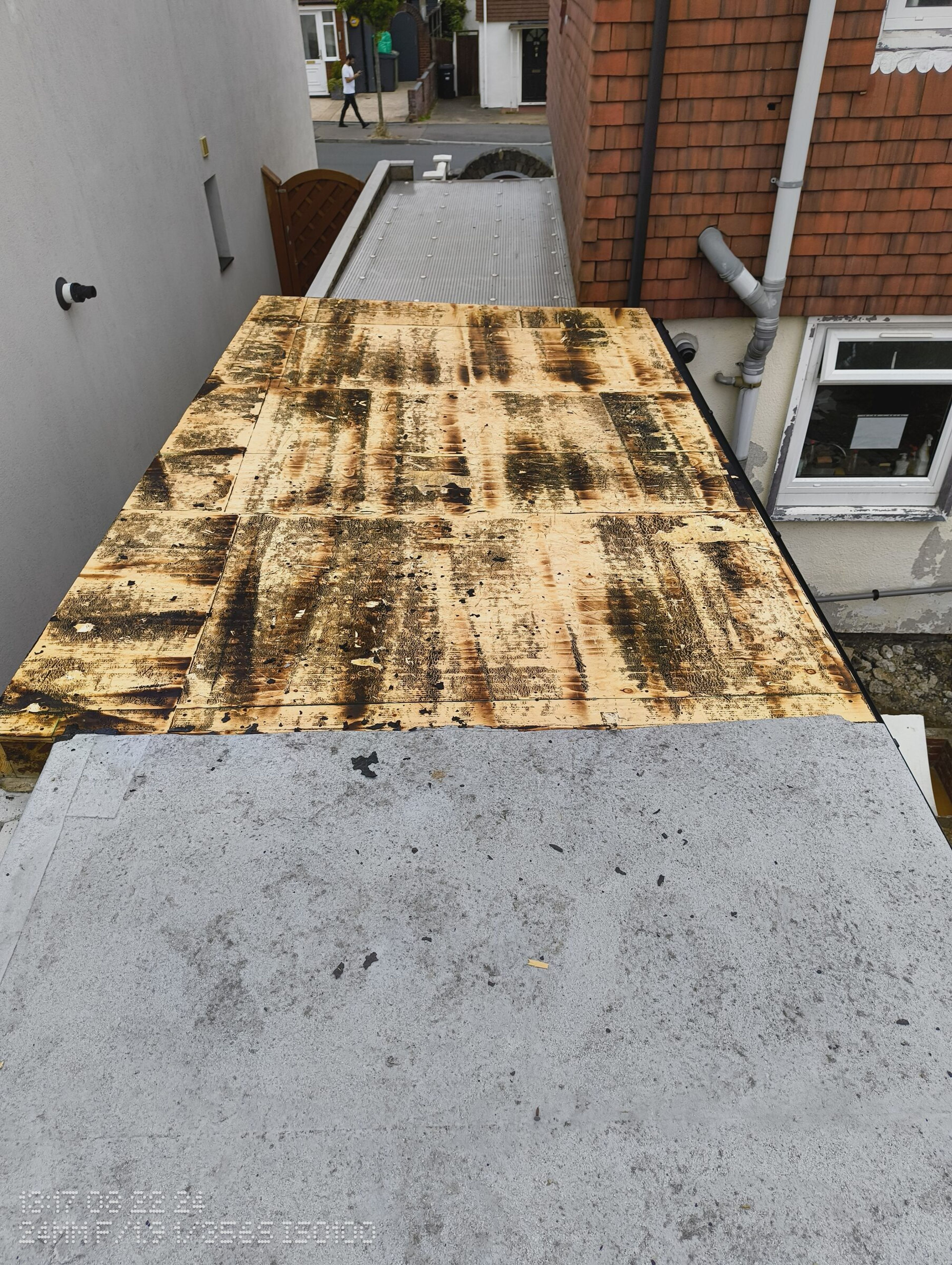 Flat roof deck fully stripped of felt, with the polycarbonate side-return roof still in place beyond it.